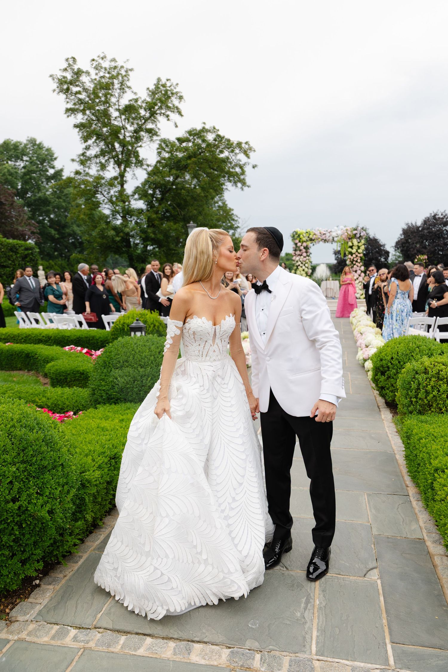 Newlyweds walking together on a garden path during an elegant outdoor wedding celebration.