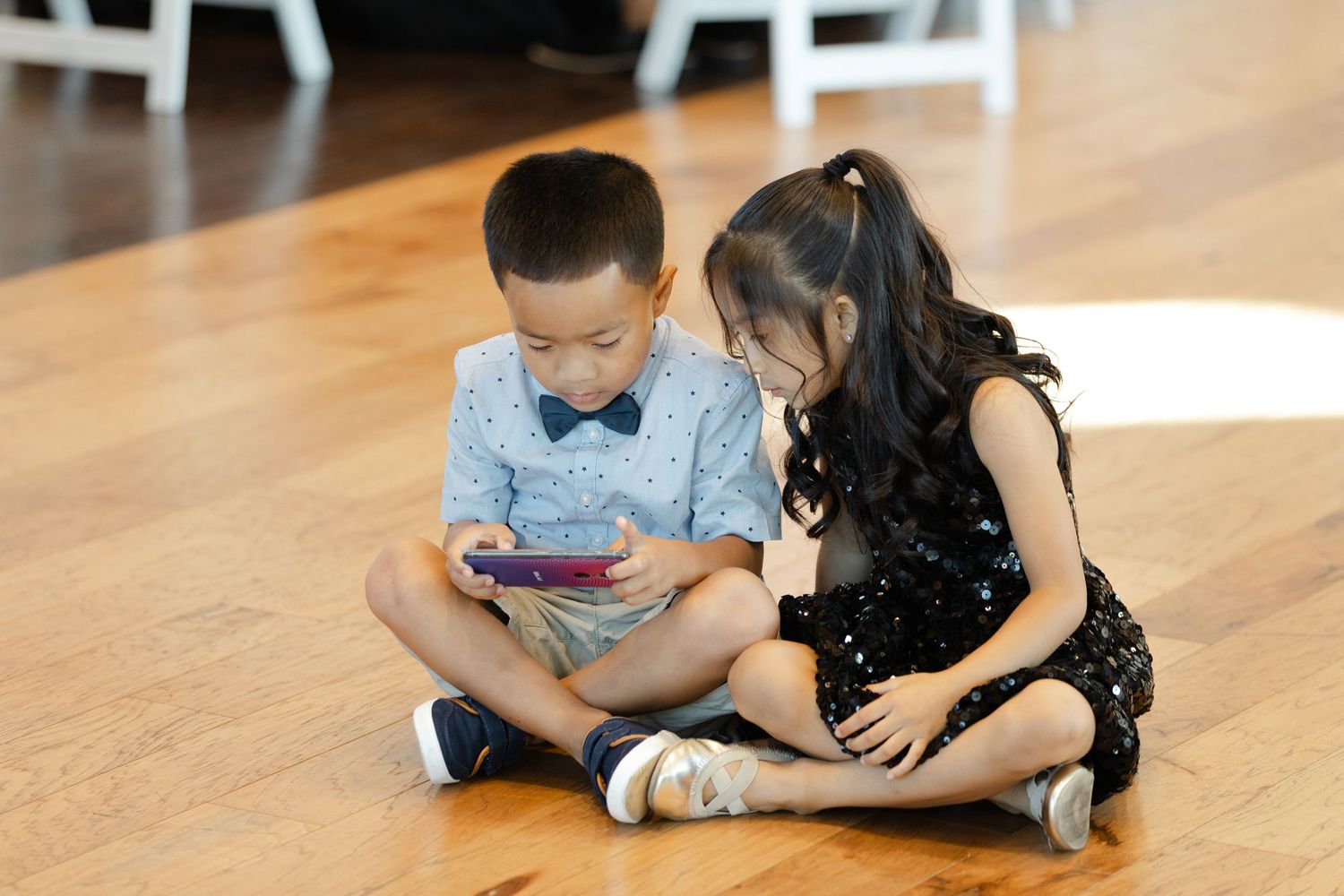 Two people lie on a wooden floor while looking at a mobile device together.