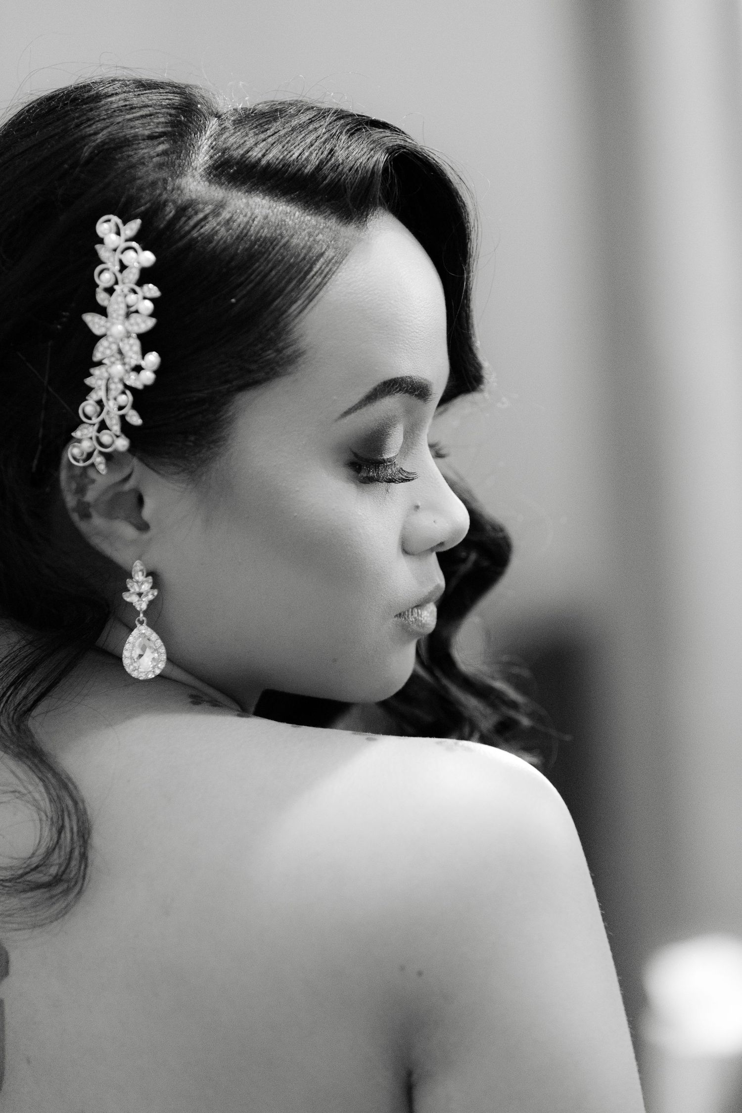 Black and white profile portrait showing elegant bridal hairstyle with crystal hair accessory and teardrop earring.