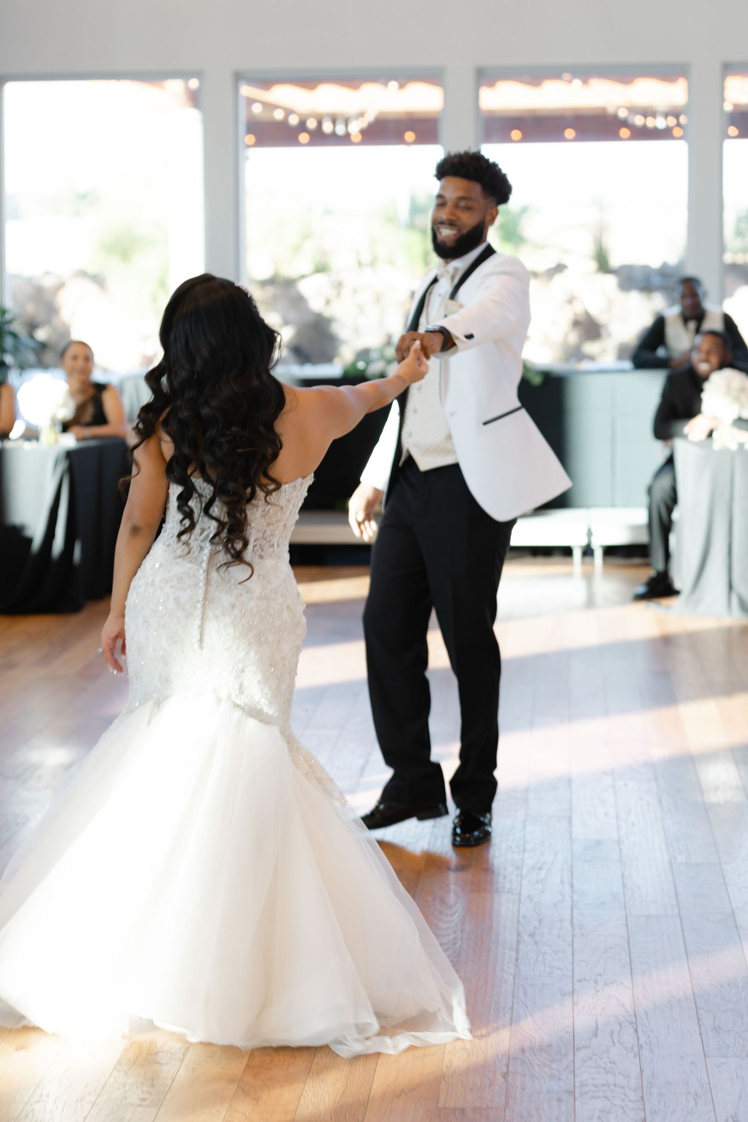 A couple performs a romantic dance move during their wedding reception on a polished wooden dance floor under string lights.
