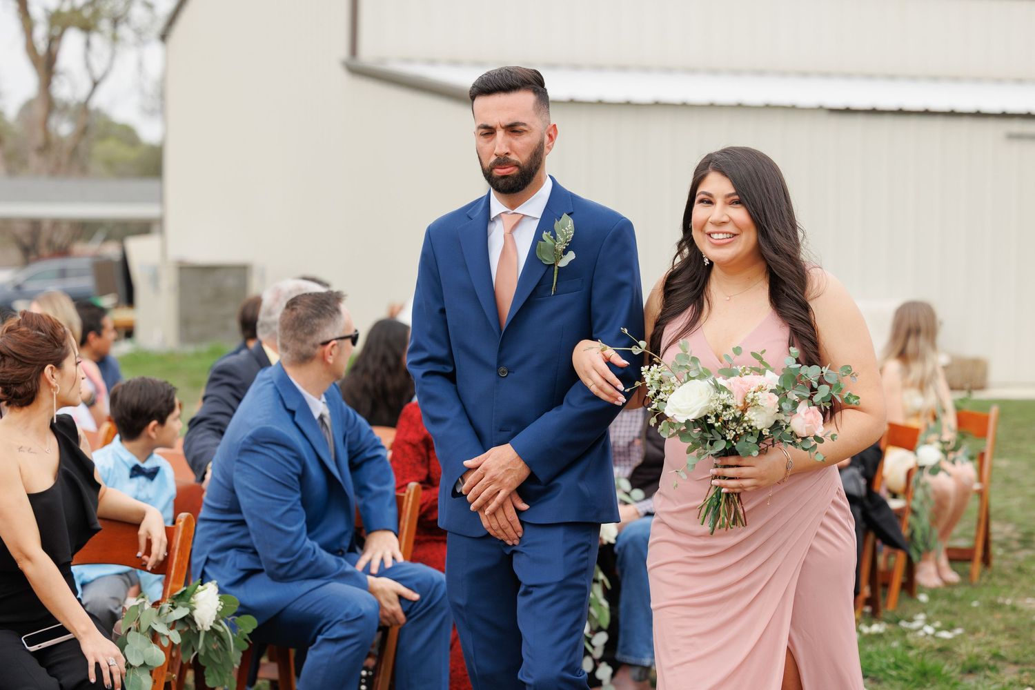 Wedding party in blue suits and blush pink dresses dance together during outdoor reception celebration.