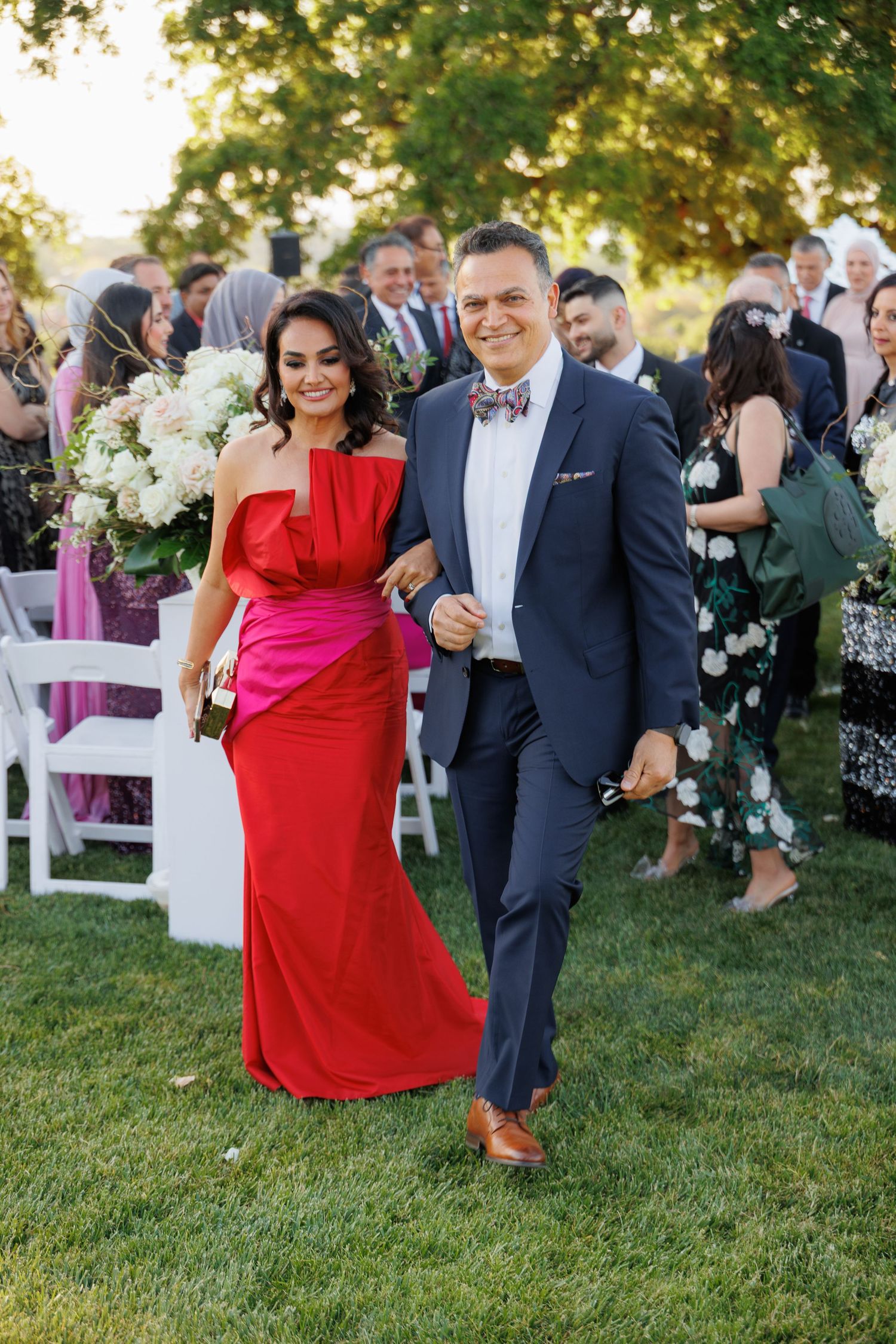 Wedding guests dancing and celebrating outdoors on a grassy lawn during a sunny afternoon reception.