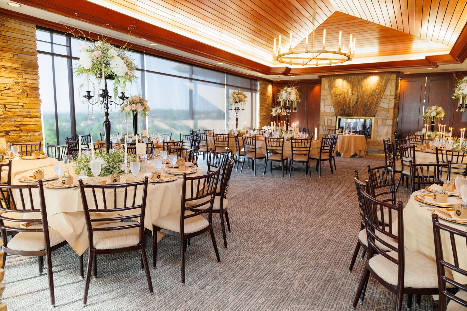 Elegant wedding reception venue with wood-paneled ceiling, round tables, and panoramic mountain views through large windows.