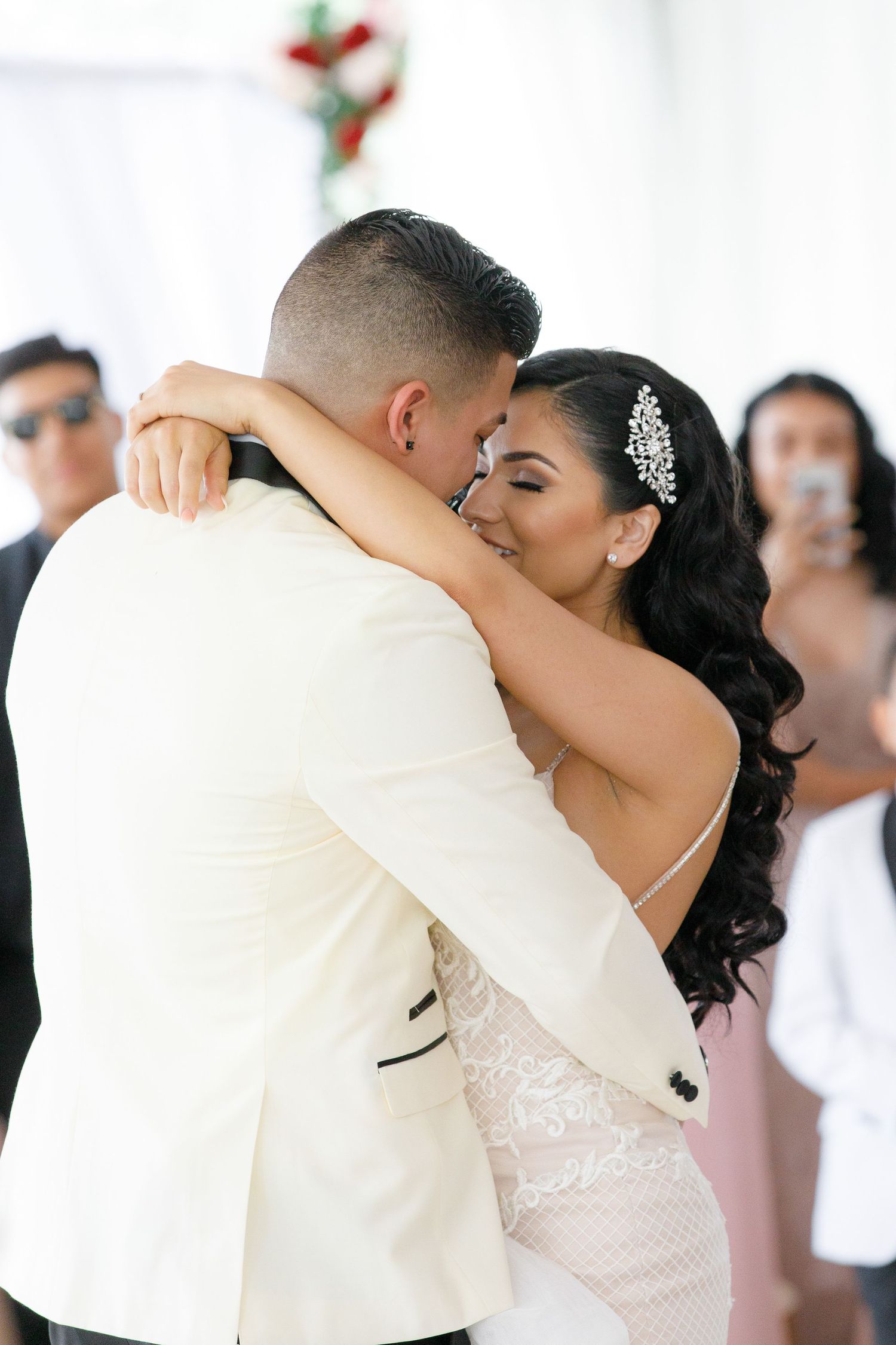 Newlywed couple shares a romantic kiss during their first dance at an elegant white wedding reception.