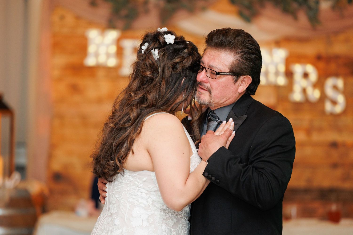 A romantic wedding couple sharing an intimate kiss in front of a rustic wooden wall with warm lighting.