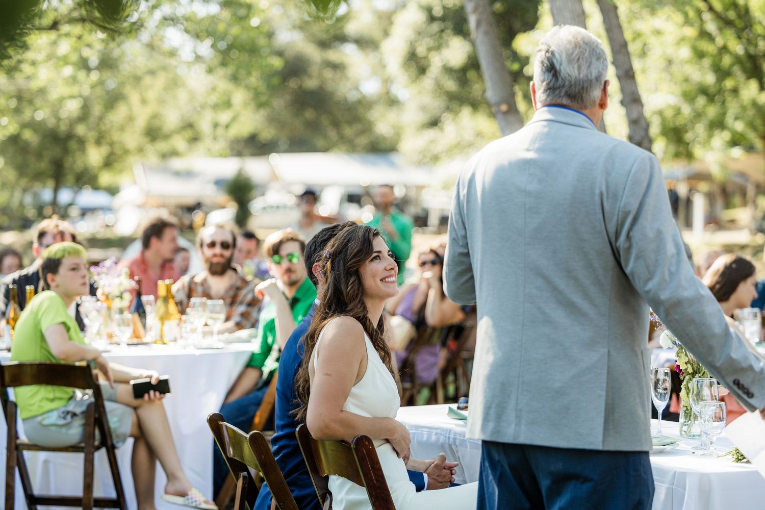 Wedding guests mingle and socialize during an outdoor reception at a sunny garden venue.