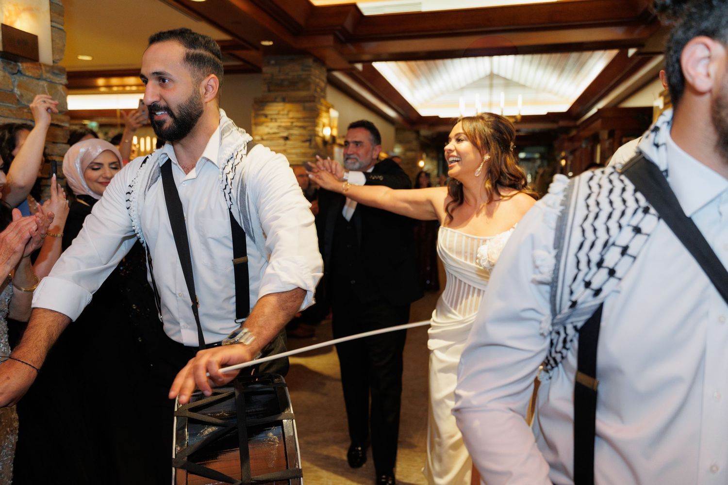 Wedding guests dancing and celebrating on a dance floor at an indoor reception venue.