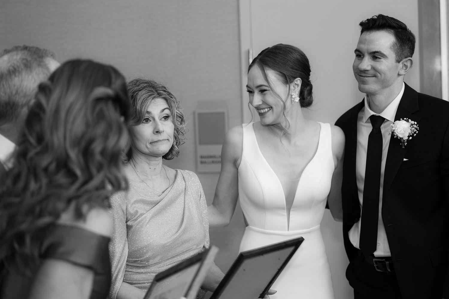 Black and white wedding photo showing bride and wedding party looking at papers during ceremony.