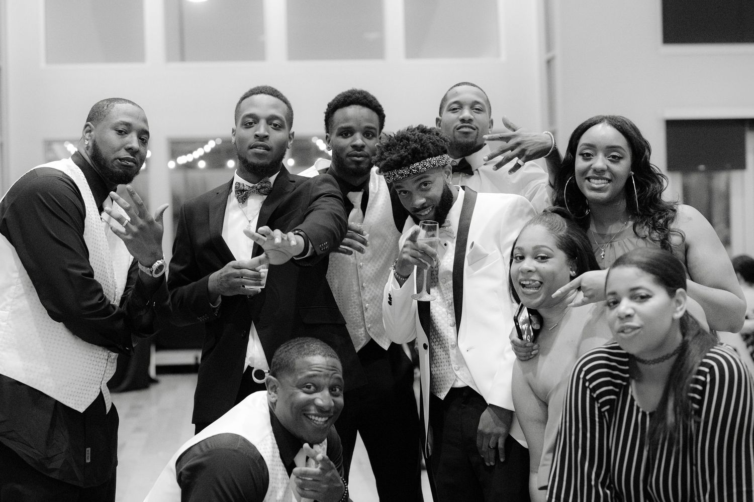 A black and white photograph shows a group of people posing together playfully at what appears to be a formal event.
