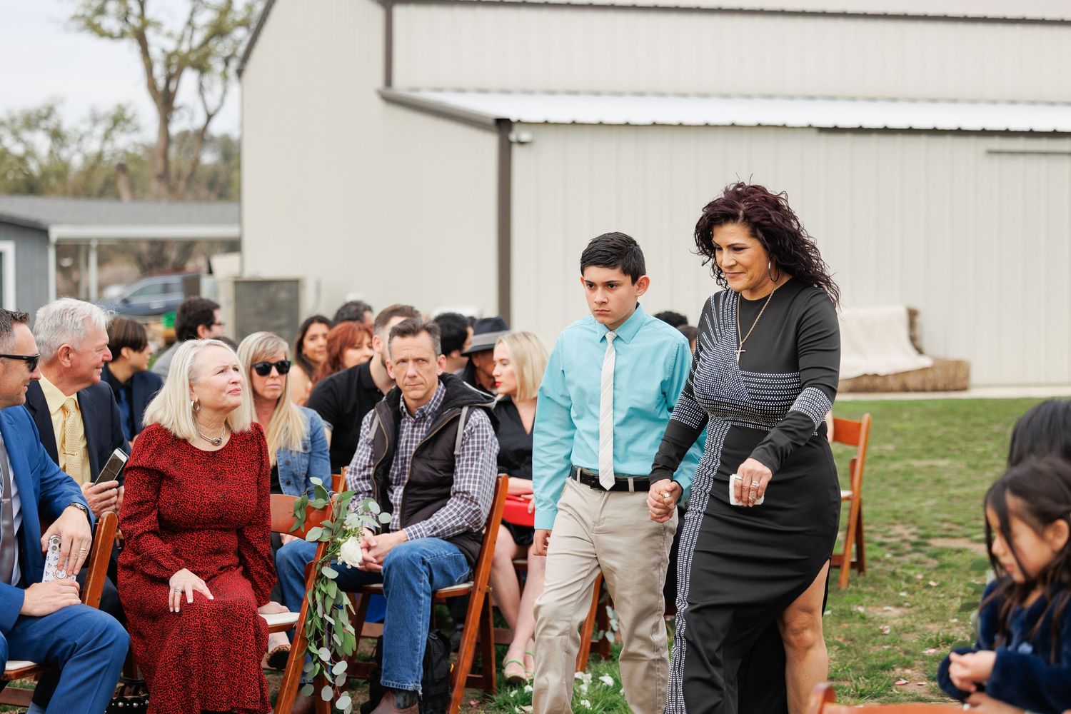 A group of people gathered outdoors at a casual event with chairs arranged on grass near a building.