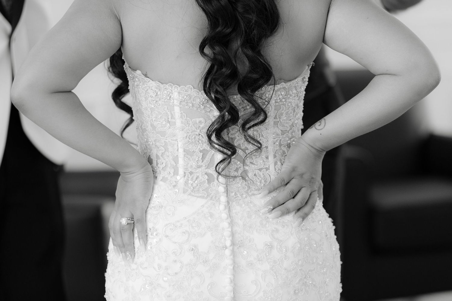 A bride in a white lace wedding dress stands elegantly while showing off intricate details of her gown.