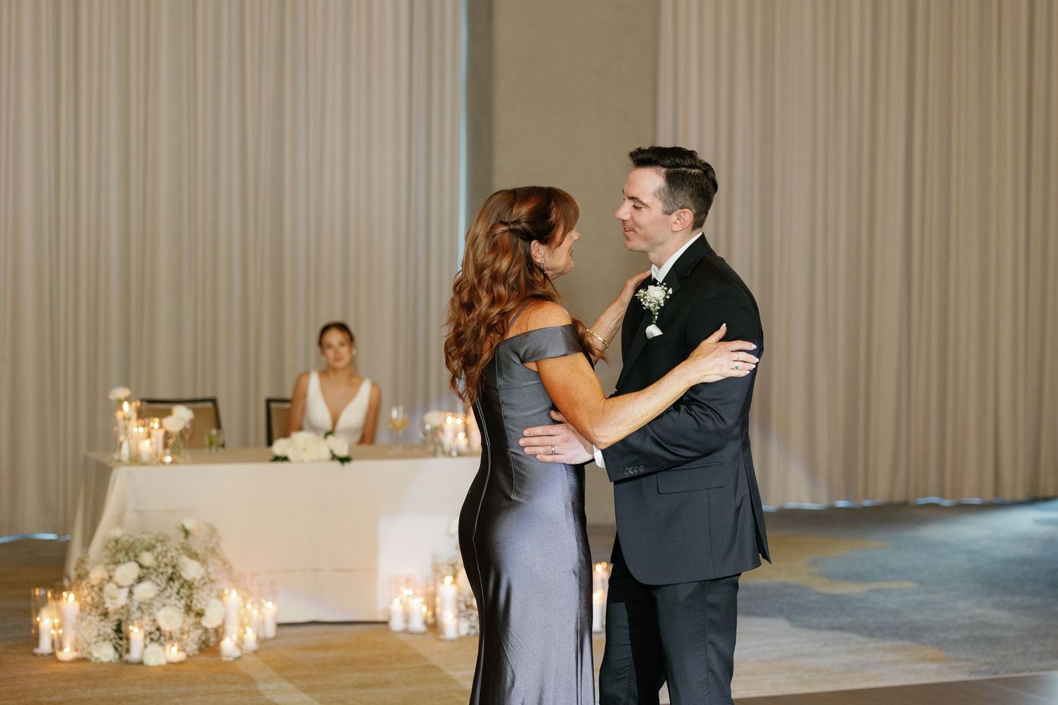 A couple shares their first dance at a wedding reception in an elegant ballroom with soft lighting and curtained walls.