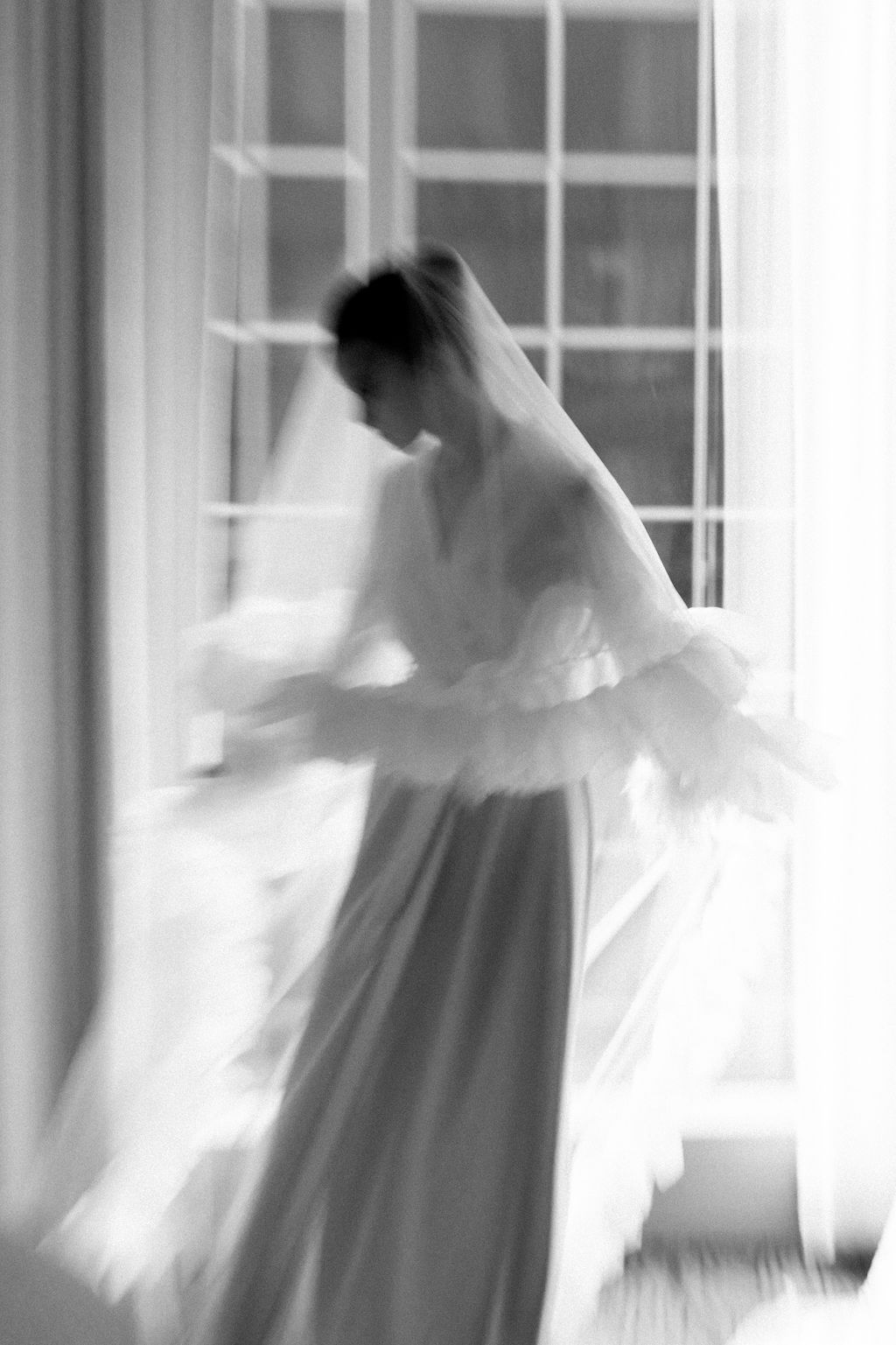 Artistic motion blur of a bride in white dress spinning near windows, creating an ethereal effect.