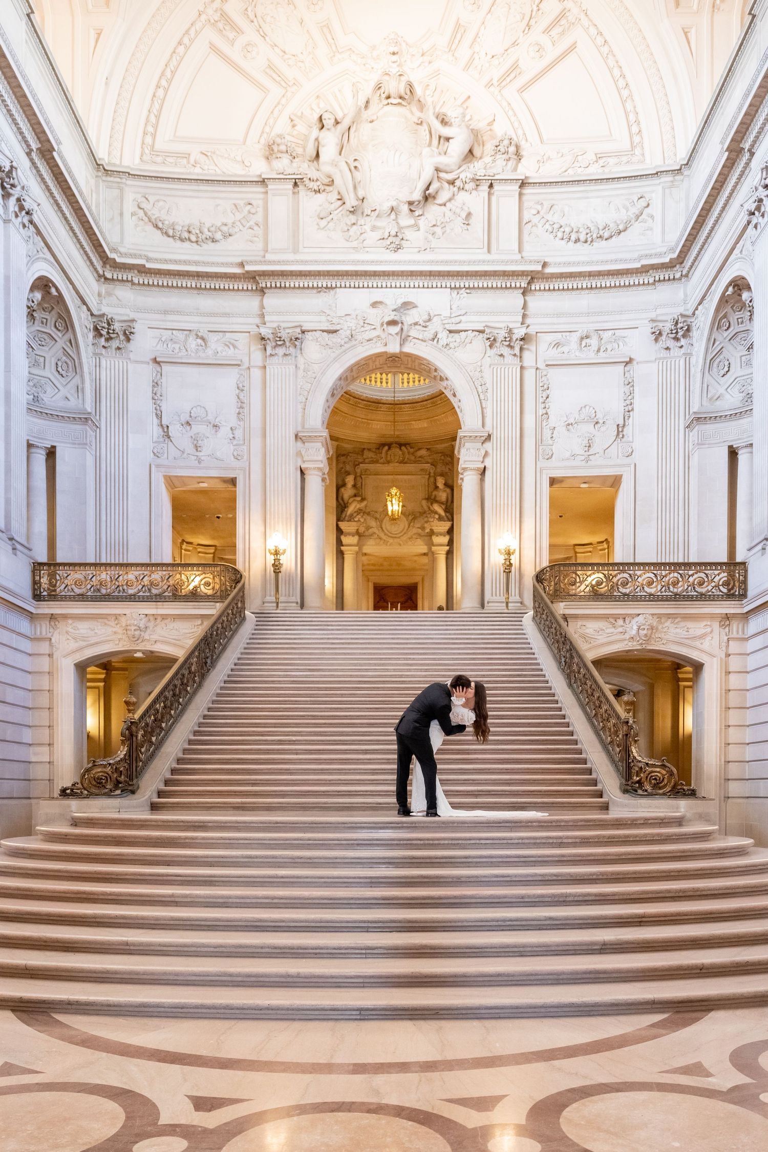 Couple sharing a romantic dip kiss on the grand staircase of San Francisco City Hall during their wedding.