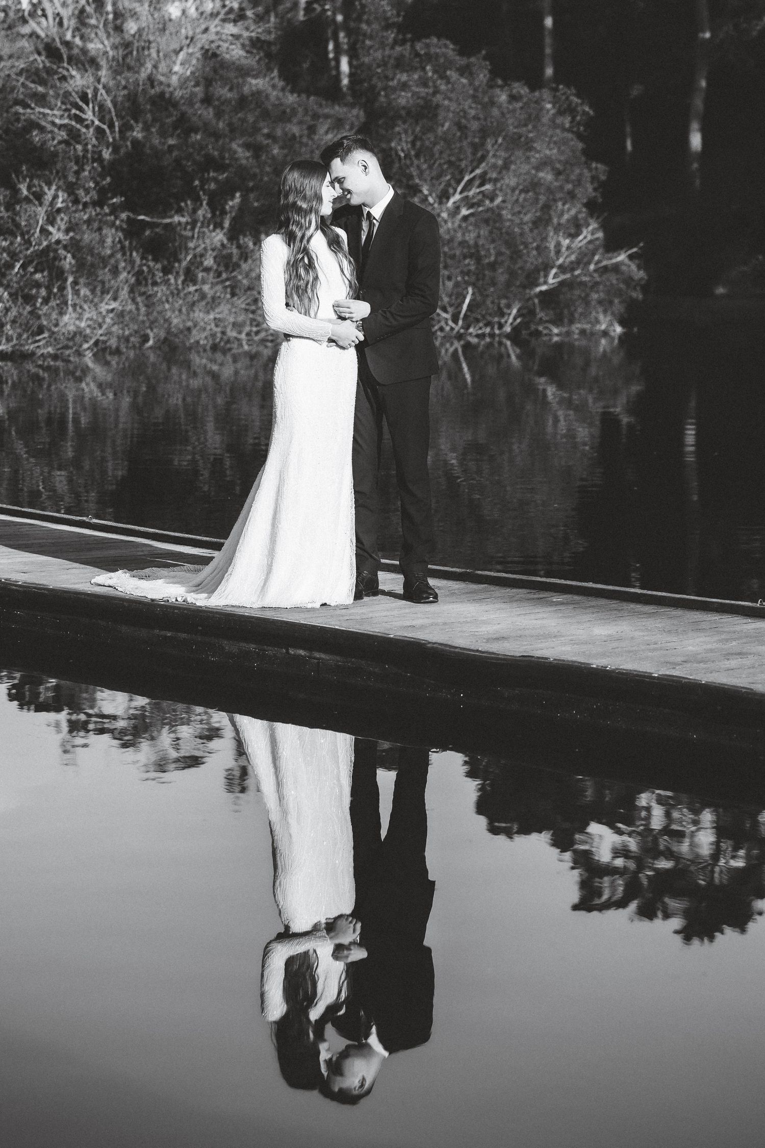 Black and white wedding reflection photo on calm water surface with dramatic symmetry.