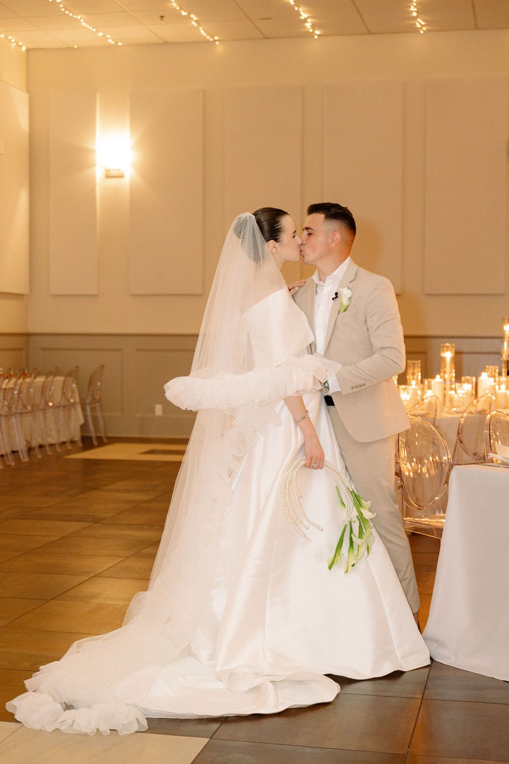 Couple sharing an intimate dance in a beautifully decorated white wedding reception hall with string lights.