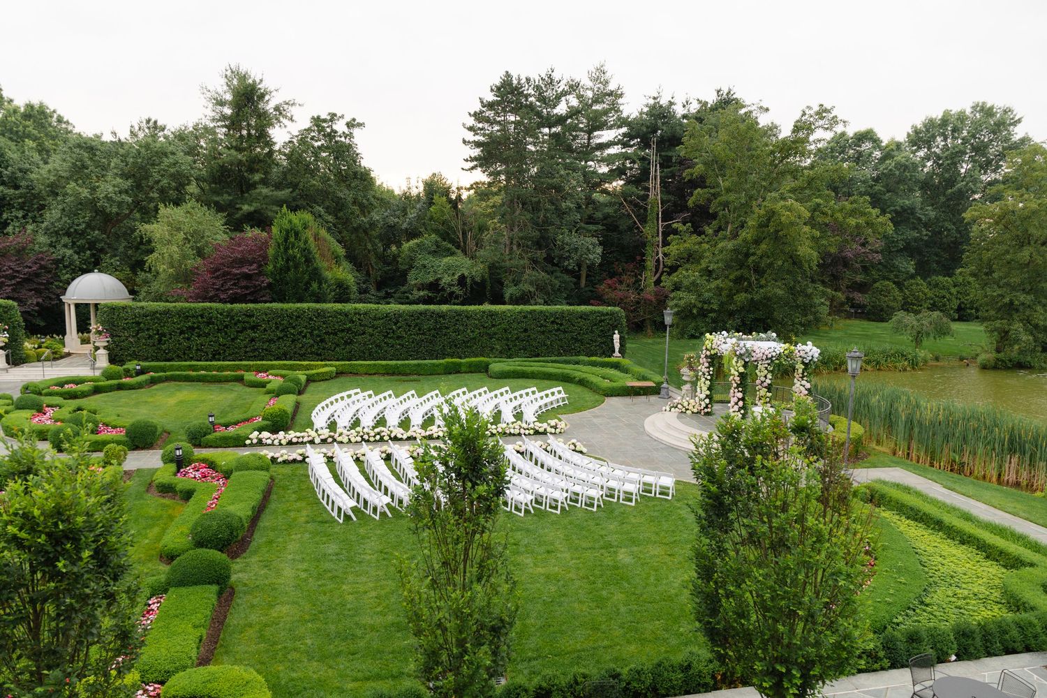 White chairs arranged in rows for an outdoor garden wedding ceremony with manicured hedges and landscaping.