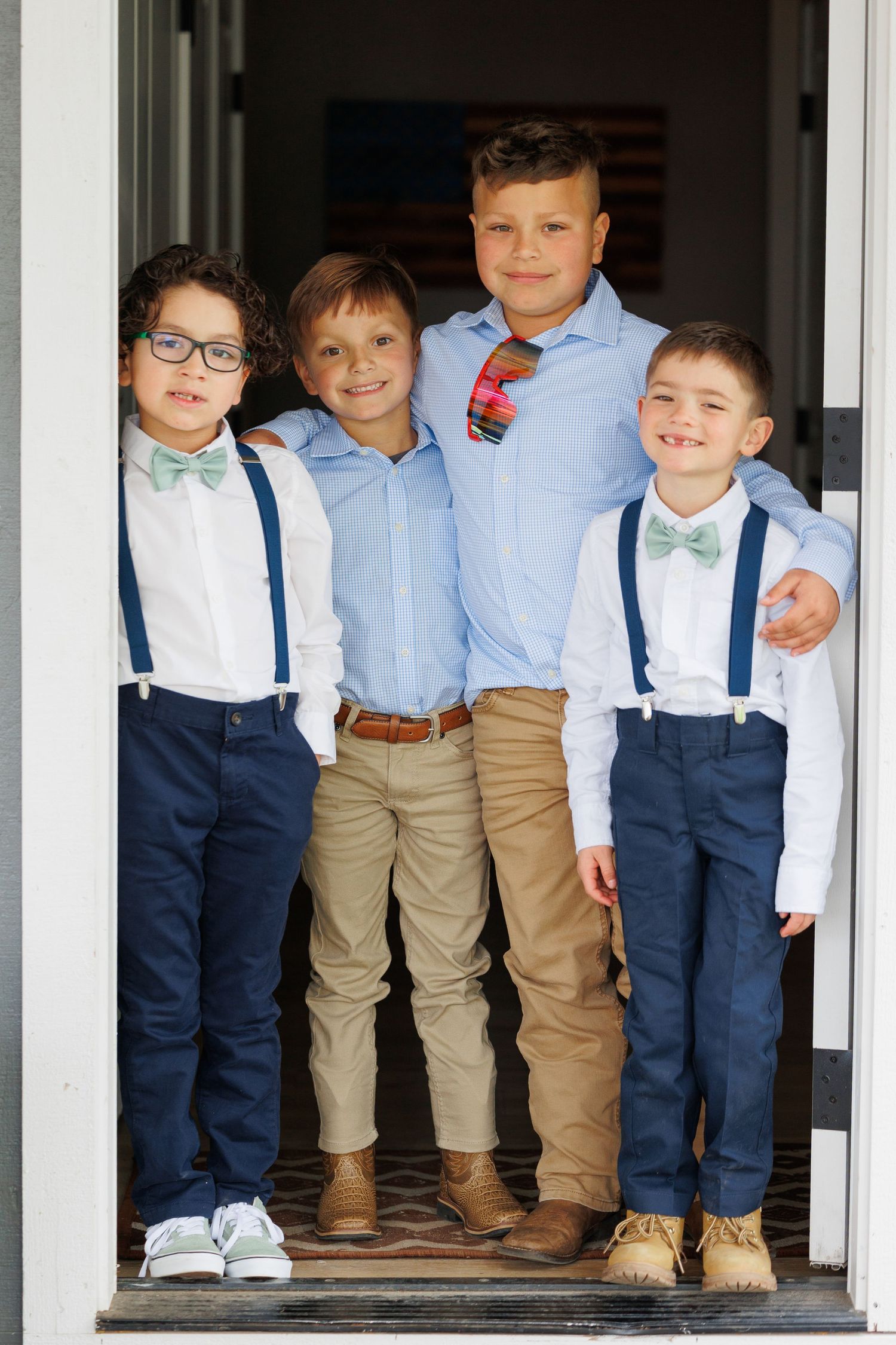 A group of young children wearing coordinated outfits with navy suspenders and light blue shirts pose together on steps.