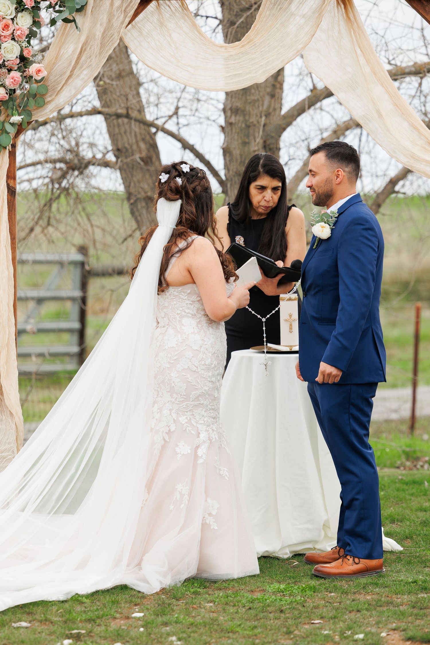 A romantic outdoor wedding ceremony under draped fabric and trees with the couple sharing intimate moments.