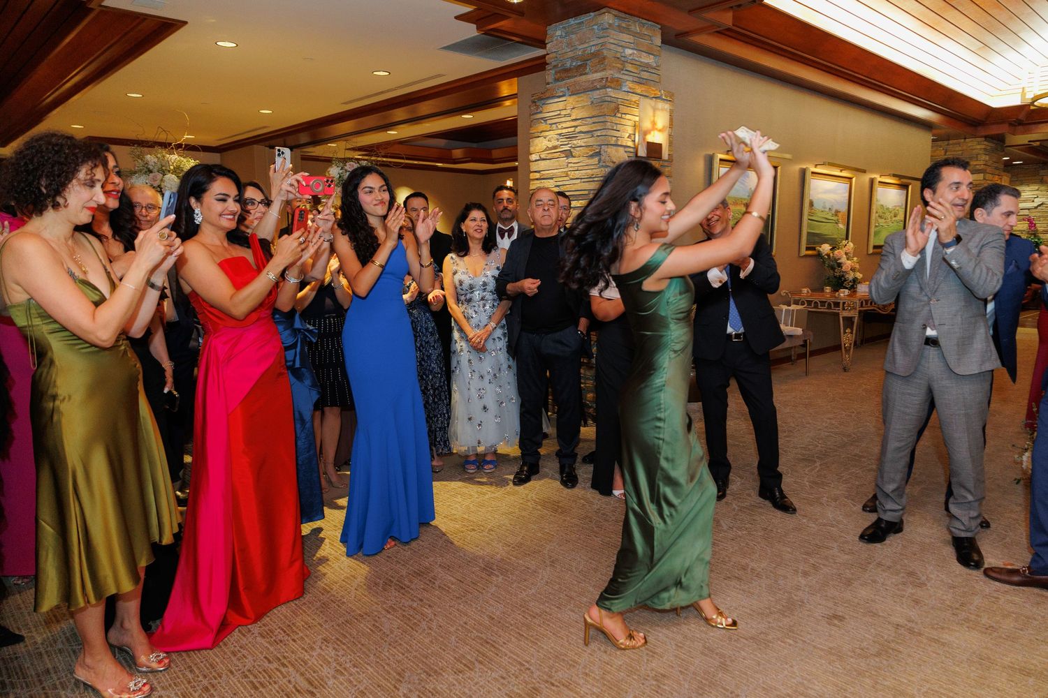 Wedding guests in colorful formal attire cheer and celebrate during a reception at an indoor venue.