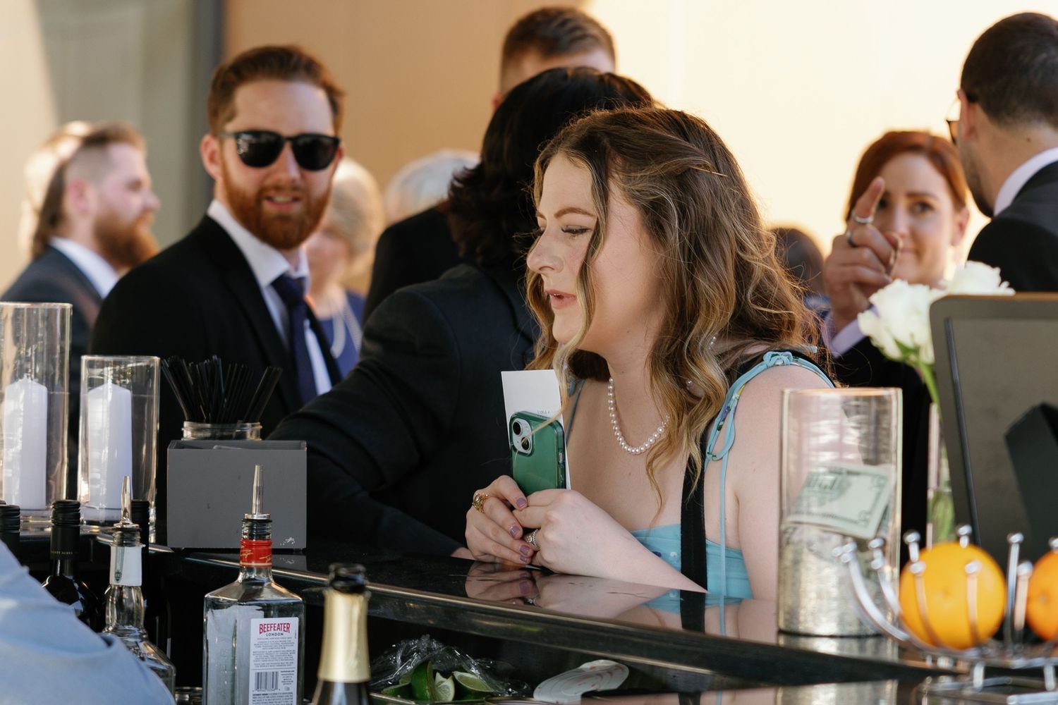 Wedding guests socialize and enjoy drinks at an elegant reception venue with natural lighting.