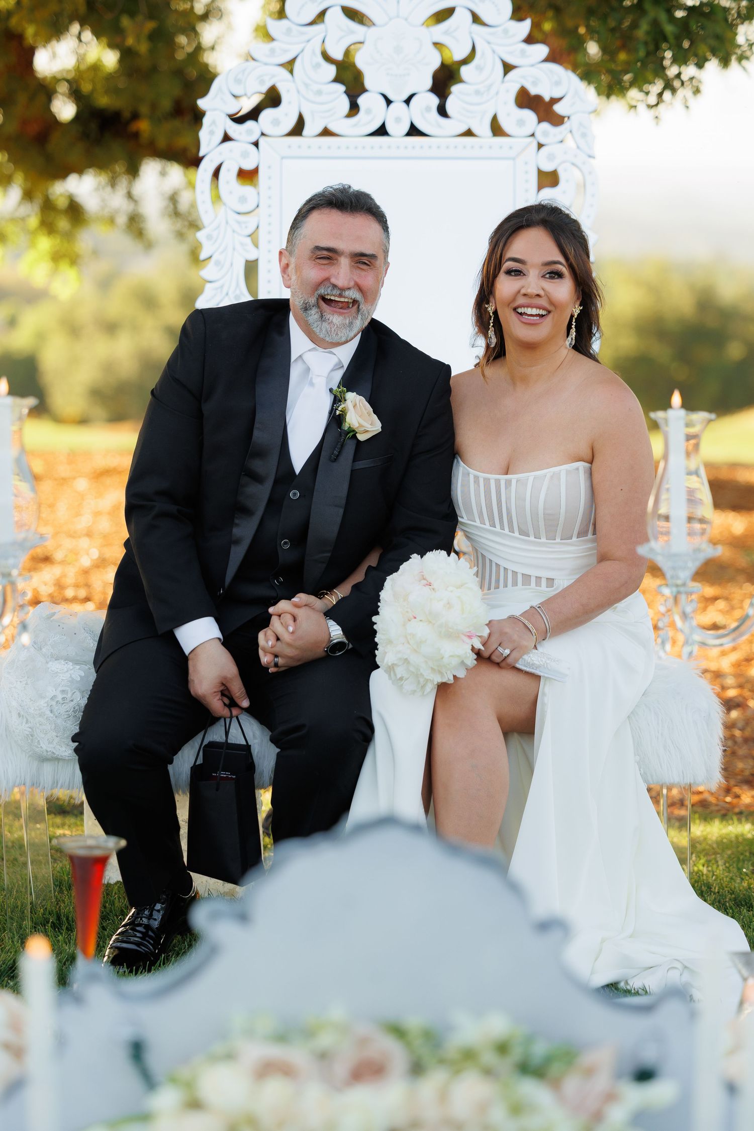 Joyful couple shares candid moments while sitting together outdoors during autumn wedding celebration.