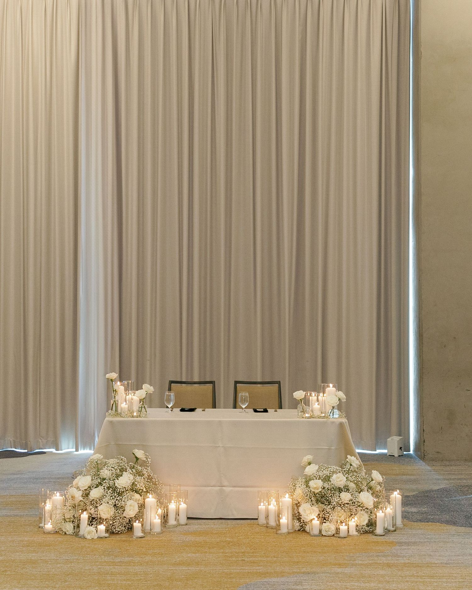 Elegant wedding reception setup with white curtains, candles, and floral arrangements along the floor.