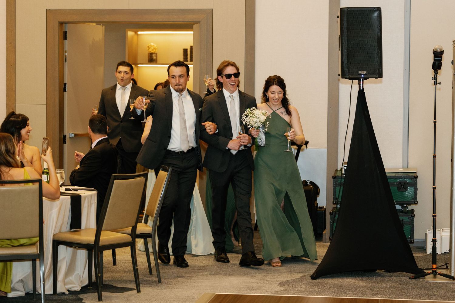 Wedding party members make their grand entrance at a reception with dancing and celebratory gestures.