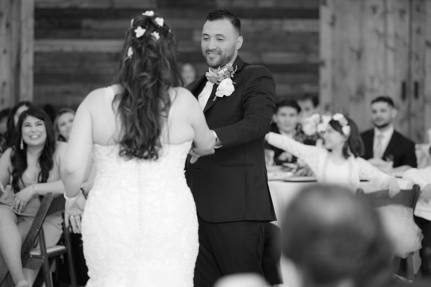 A couple shares their first dance at a wedding reception while guests watch and smile in the background.