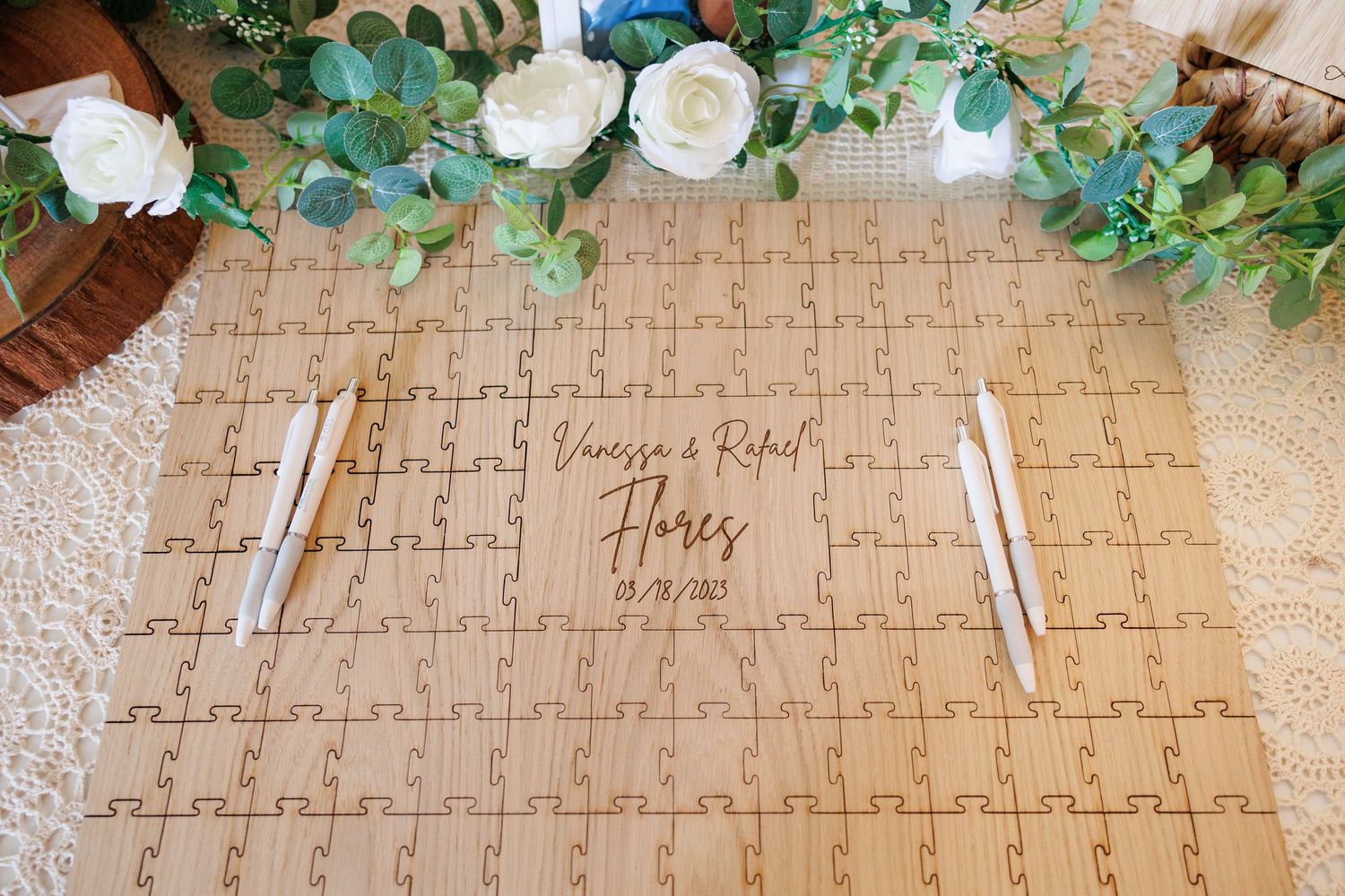 Wedding guest book made from puzzle pieces laid out on burlap fabric with greenery decorations and pens.