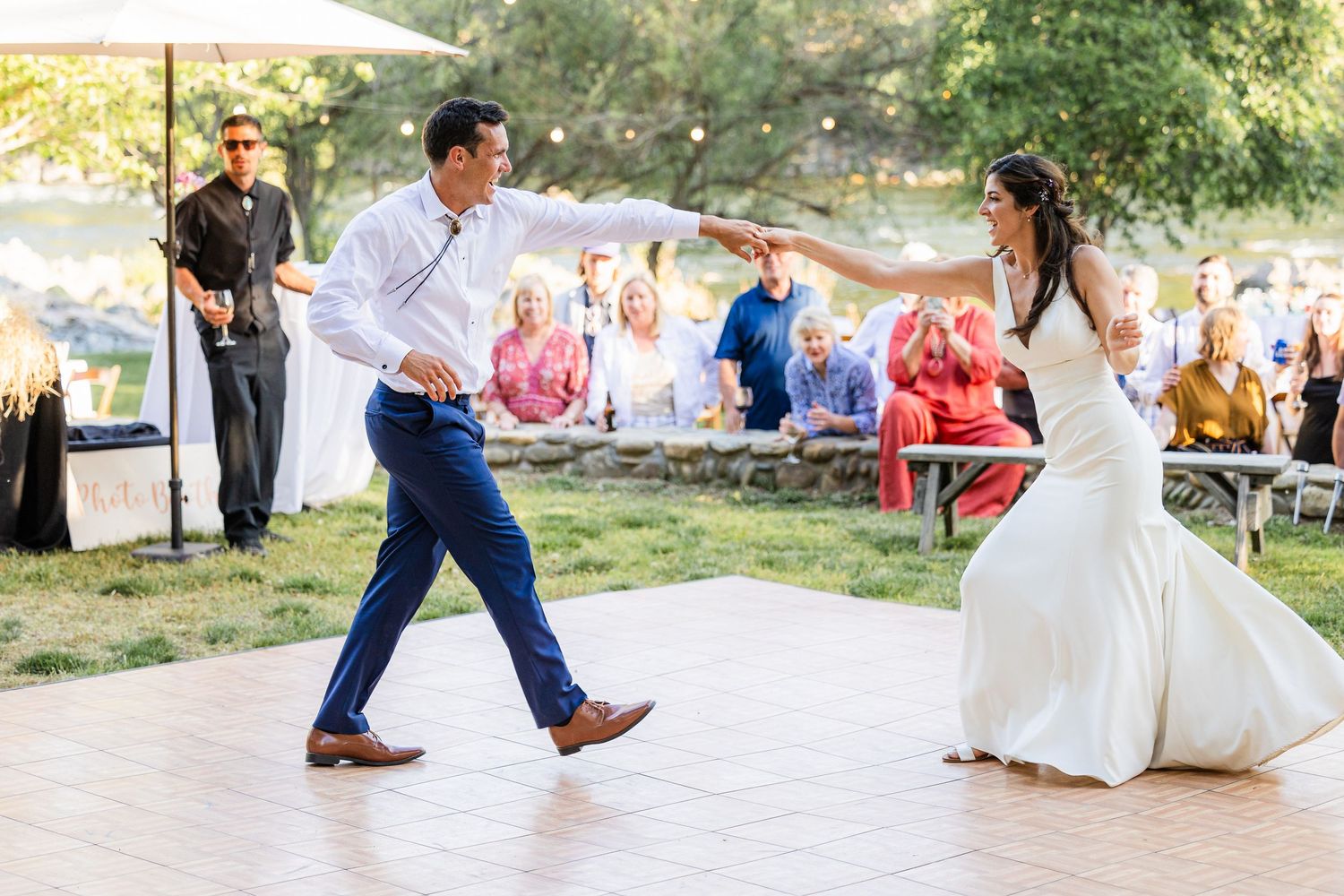 A couple performs a playful dance move during their outdoor wedding celebration on a sunny day.