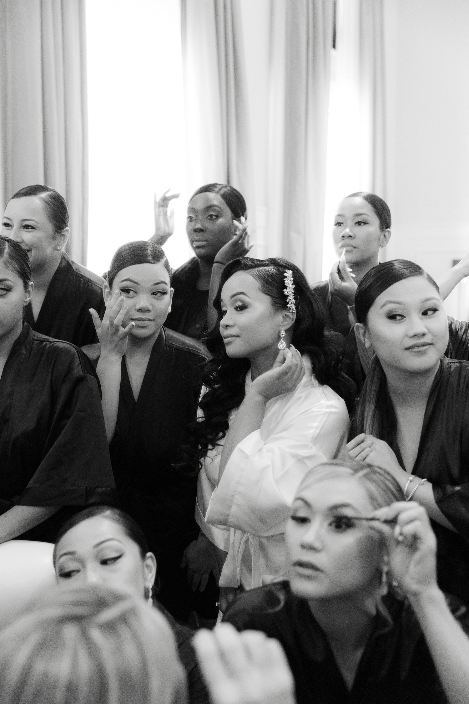 Black and white photo sequence showing models getting makeup applied backstage at a fashion event.