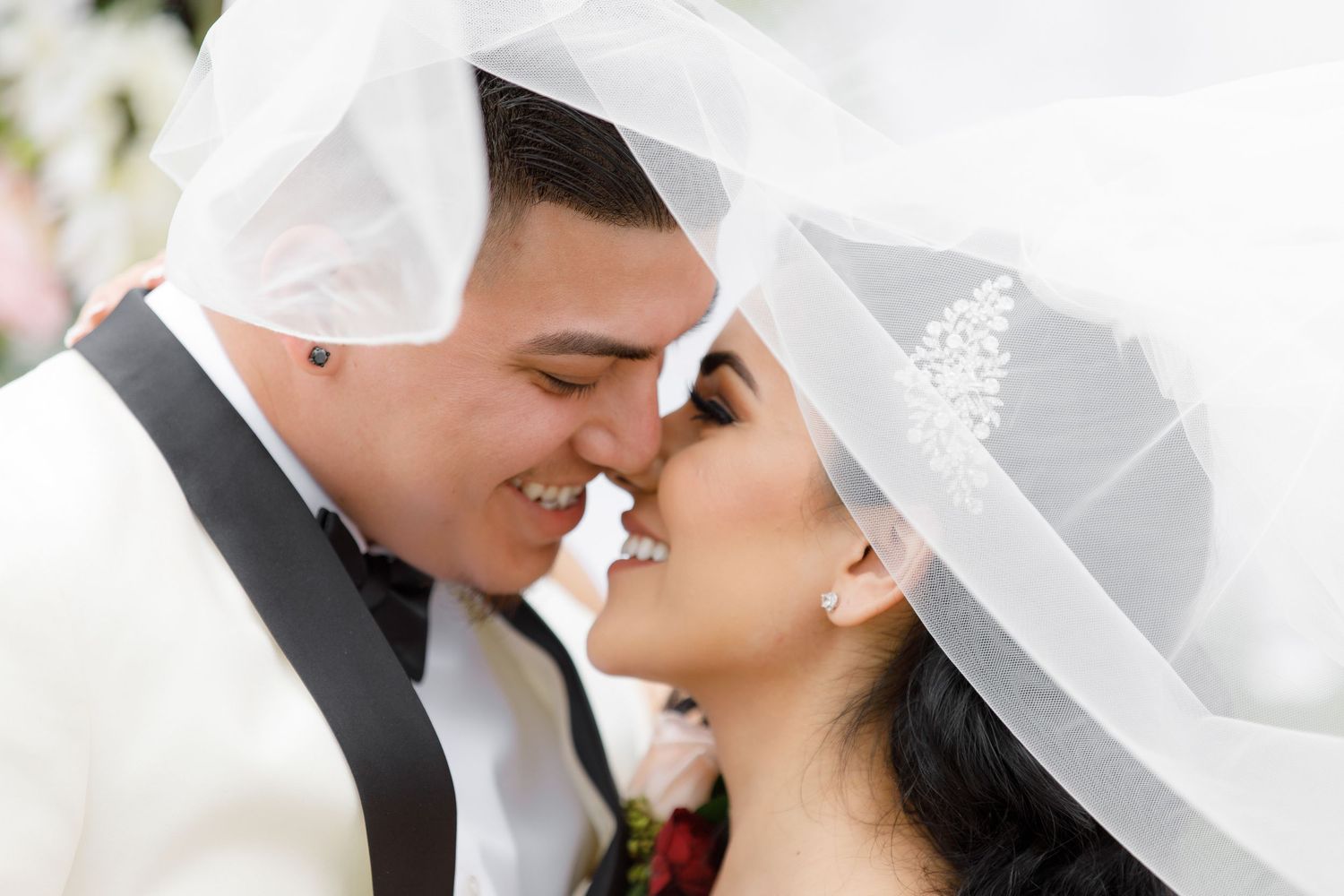 A romantic wedding couple shares a tender kiss under a white veil during their special day.