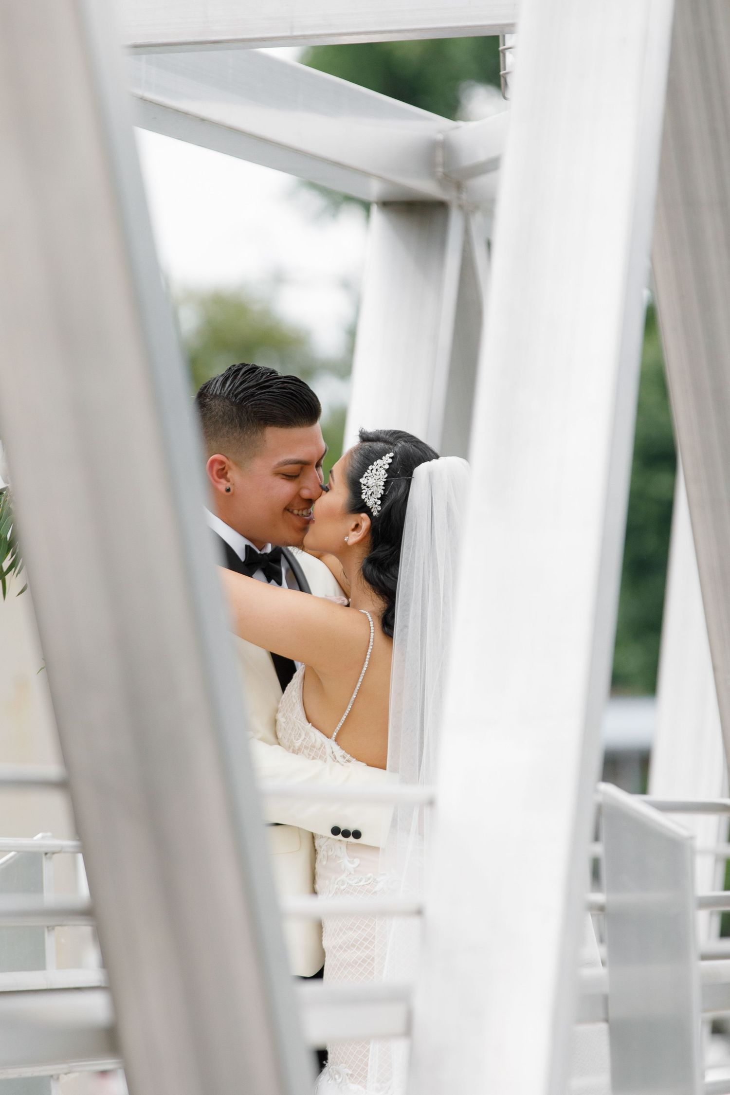 A romantic wedding couple shares an intimate moment on a white bridge structure outdoors.