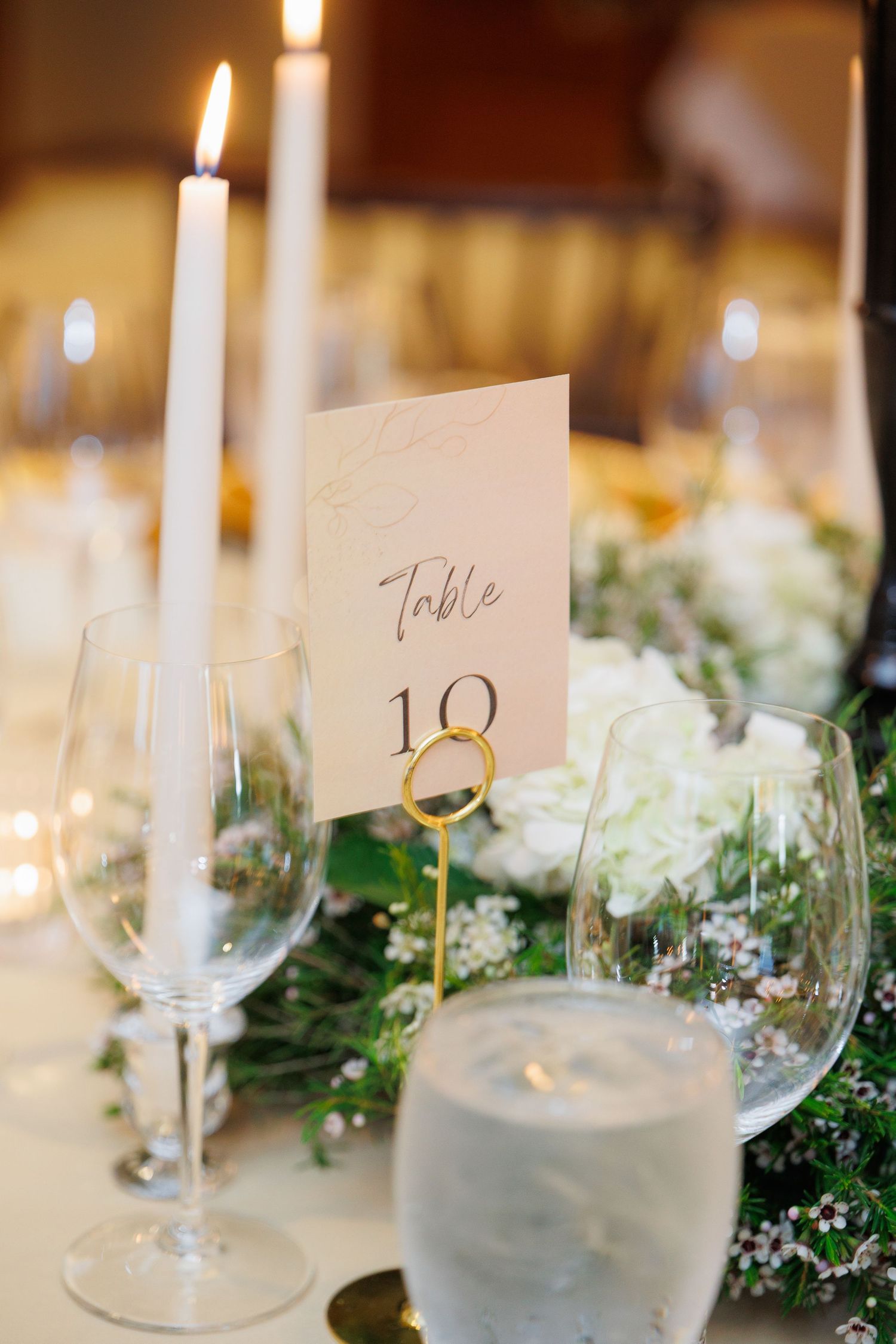 Elegant wedding reception table setting with white candles, wine glasses, and delicate floral arrangements.
