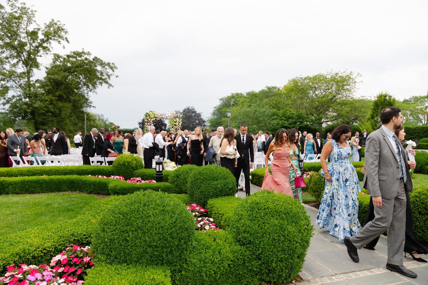 Elegant outdoor wedding ceremony in a formal garden with manicured hedges, colorful flowers, and guests in formal attire.