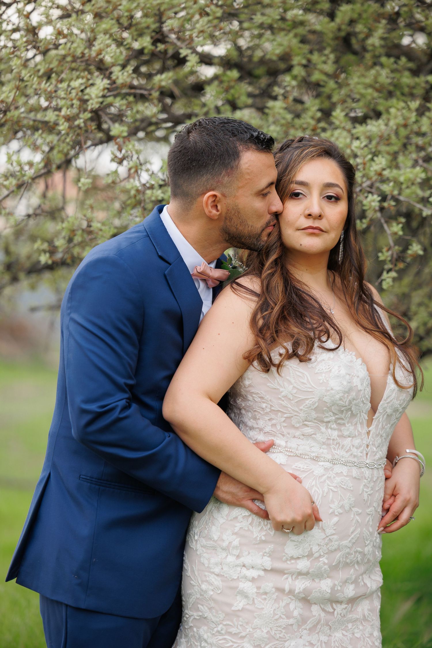 A romantic couple poses together outdoors with blooming spring trees in the background.