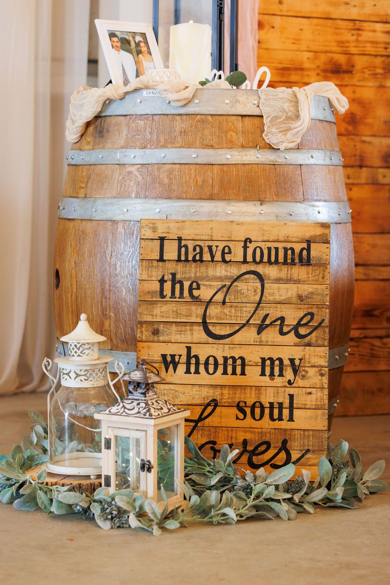 Rustic wooden barrel decorated with romantic quote, lanterns, and eucalyptus garland for wedding decor.