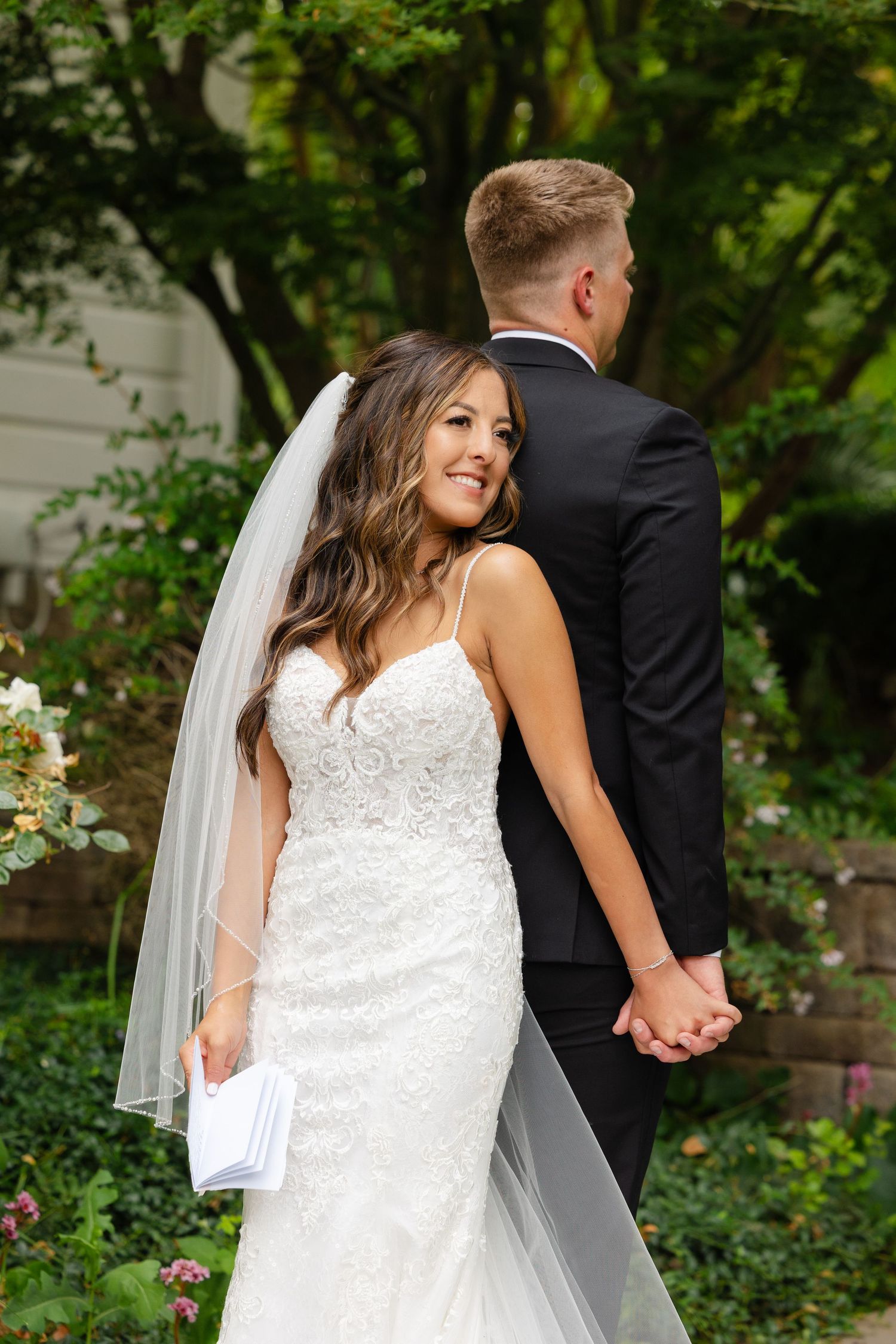 Bride and groom hold hands while walking through a lush garden setting in romantic wedding portraits.