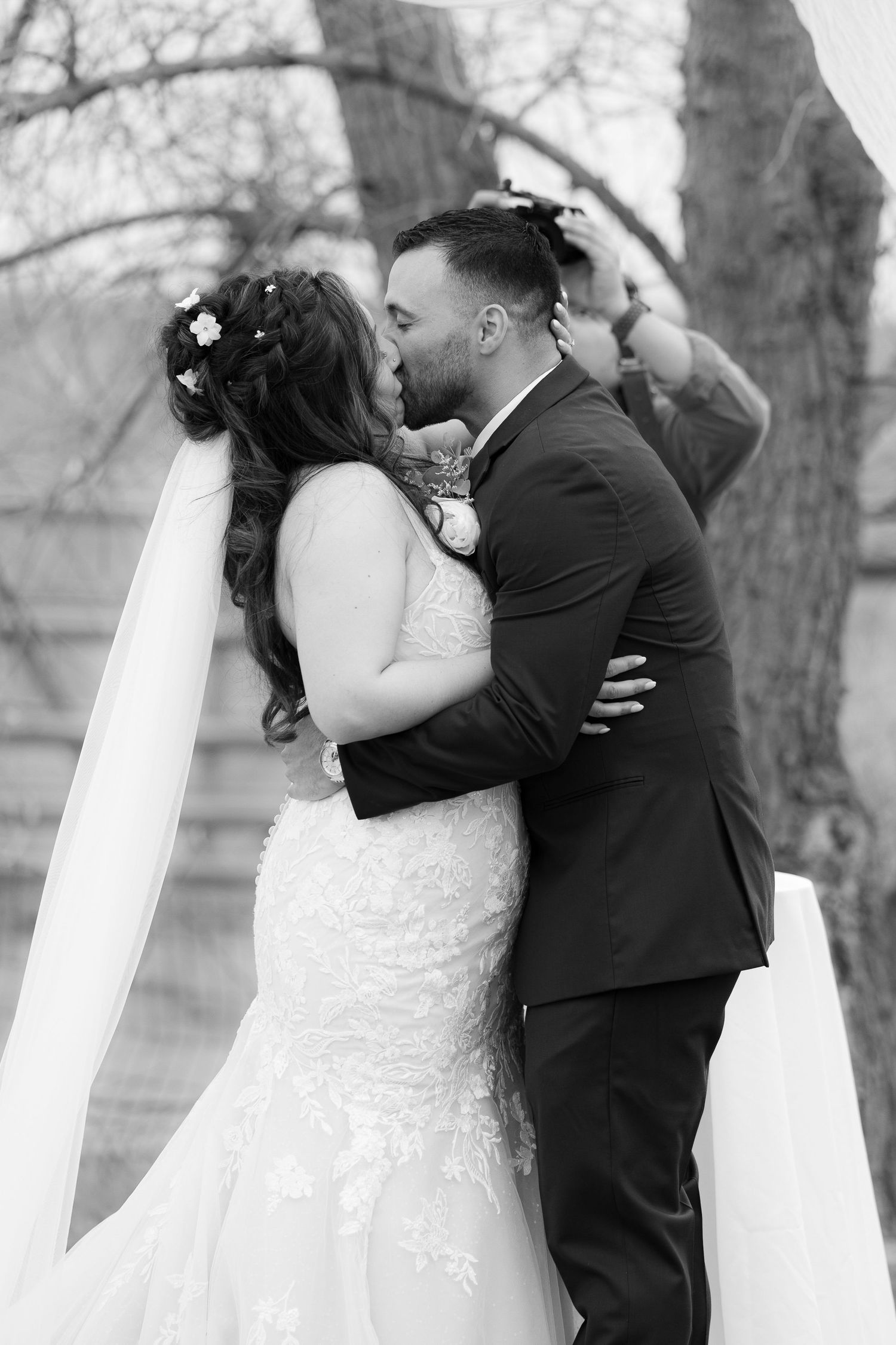 A series of four black and white wedding photos showing a couple sharing romantic kisses under bare winter trees.