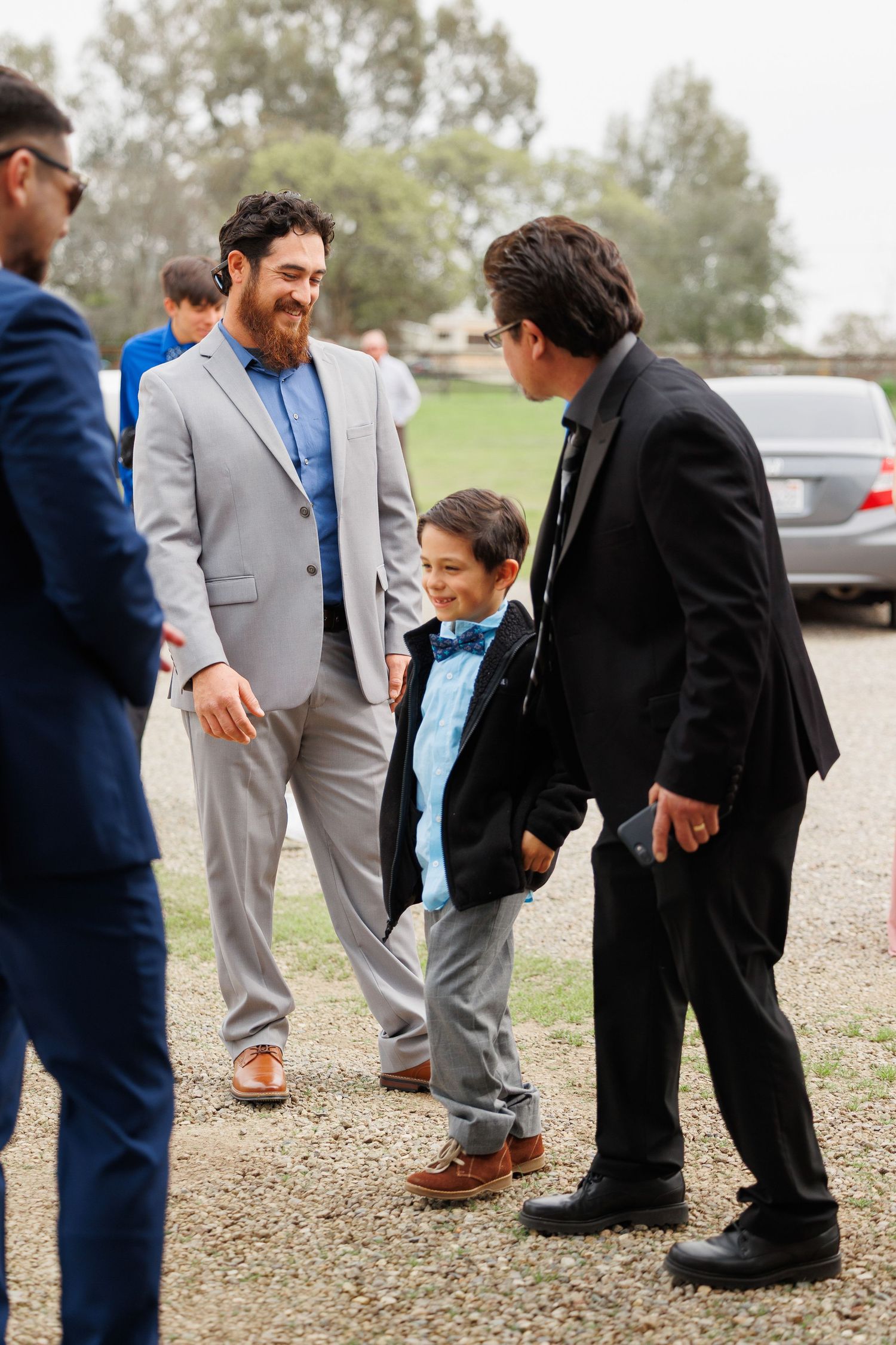 A series of candid photos showing people in formal attire interacting at an outdoor gathering on gravel ground.
