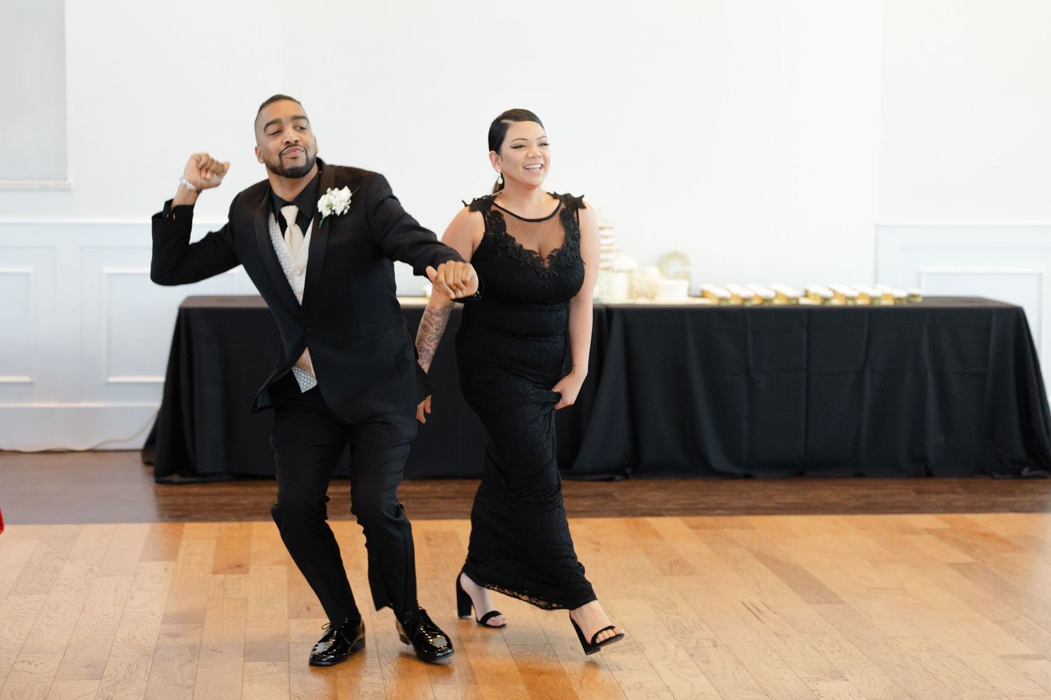 Two performers in formal black attire dance together in a bright studio space.
