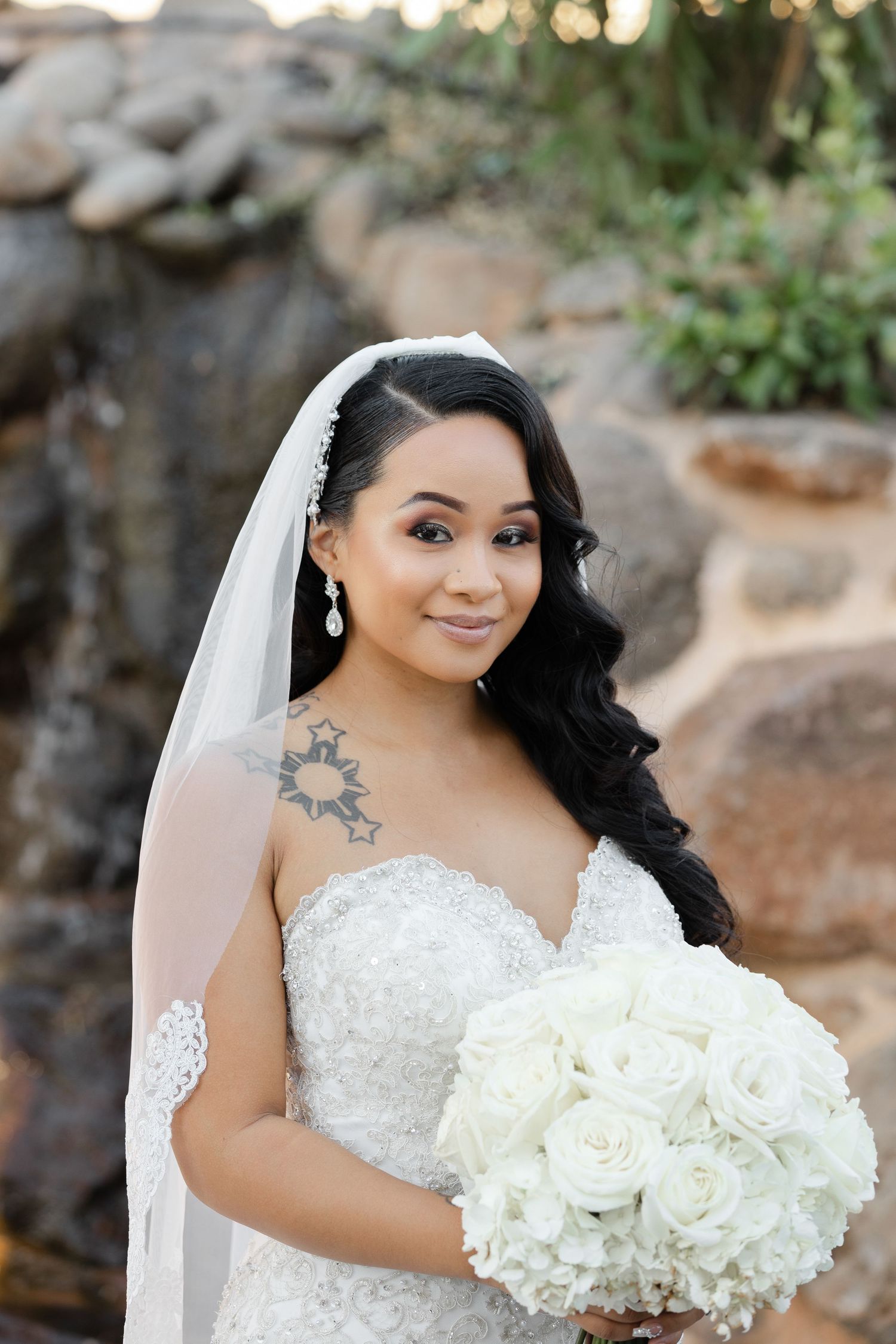 Beautiful bride in strapless lace wedding gown holds elegant white rose bouquet during outdoor portrait session.