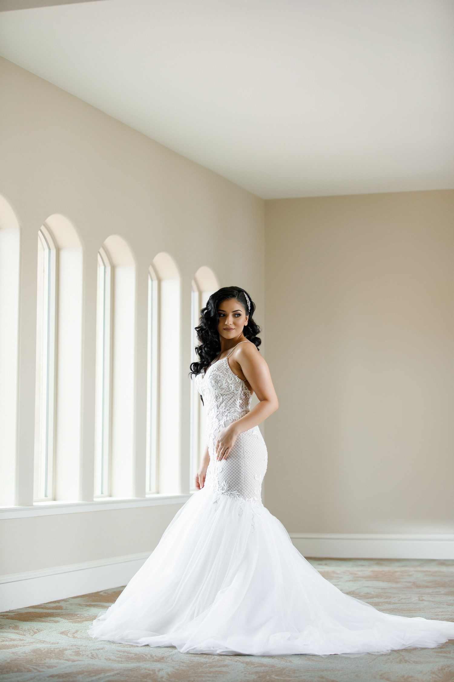 A bride in a white ballgown wedding dress poses elegantly in a bright, minimalist room with large windows.