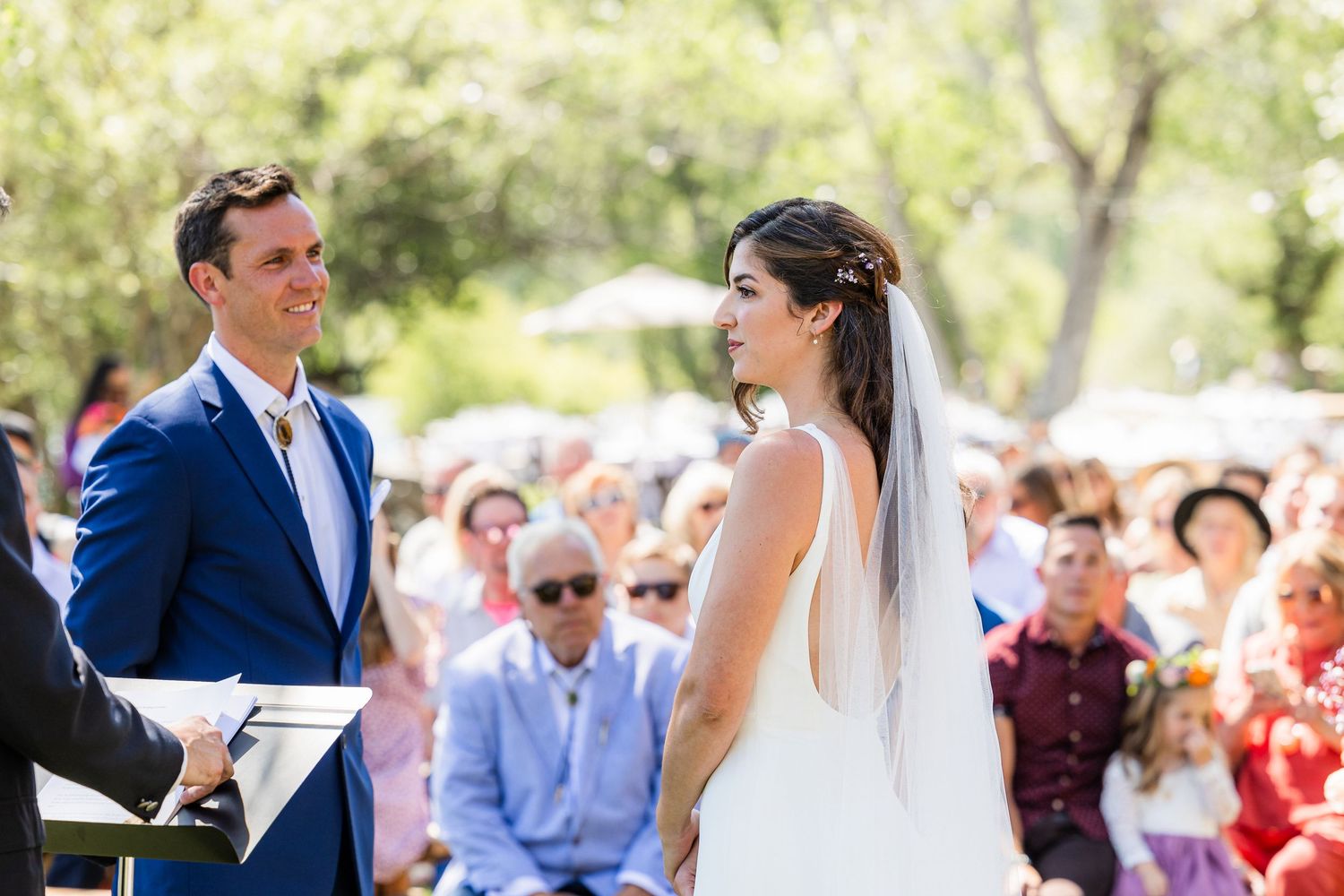 Bride and groom share a joyful moment during an outdoor wedding ceremony surrounded by guests.