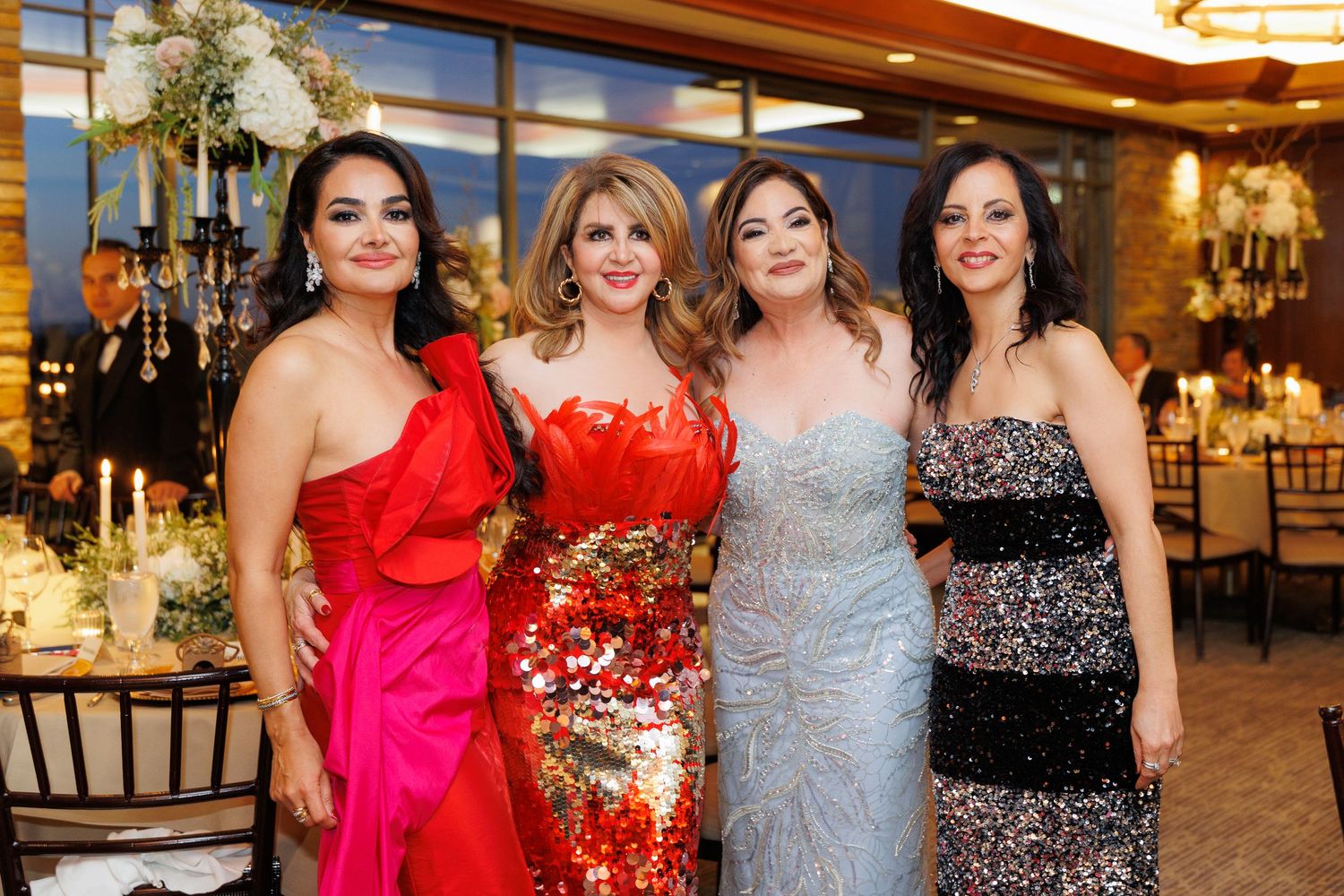 A group of people in formal attire posing together at an elegant event with warm lighting and decorative interiors.