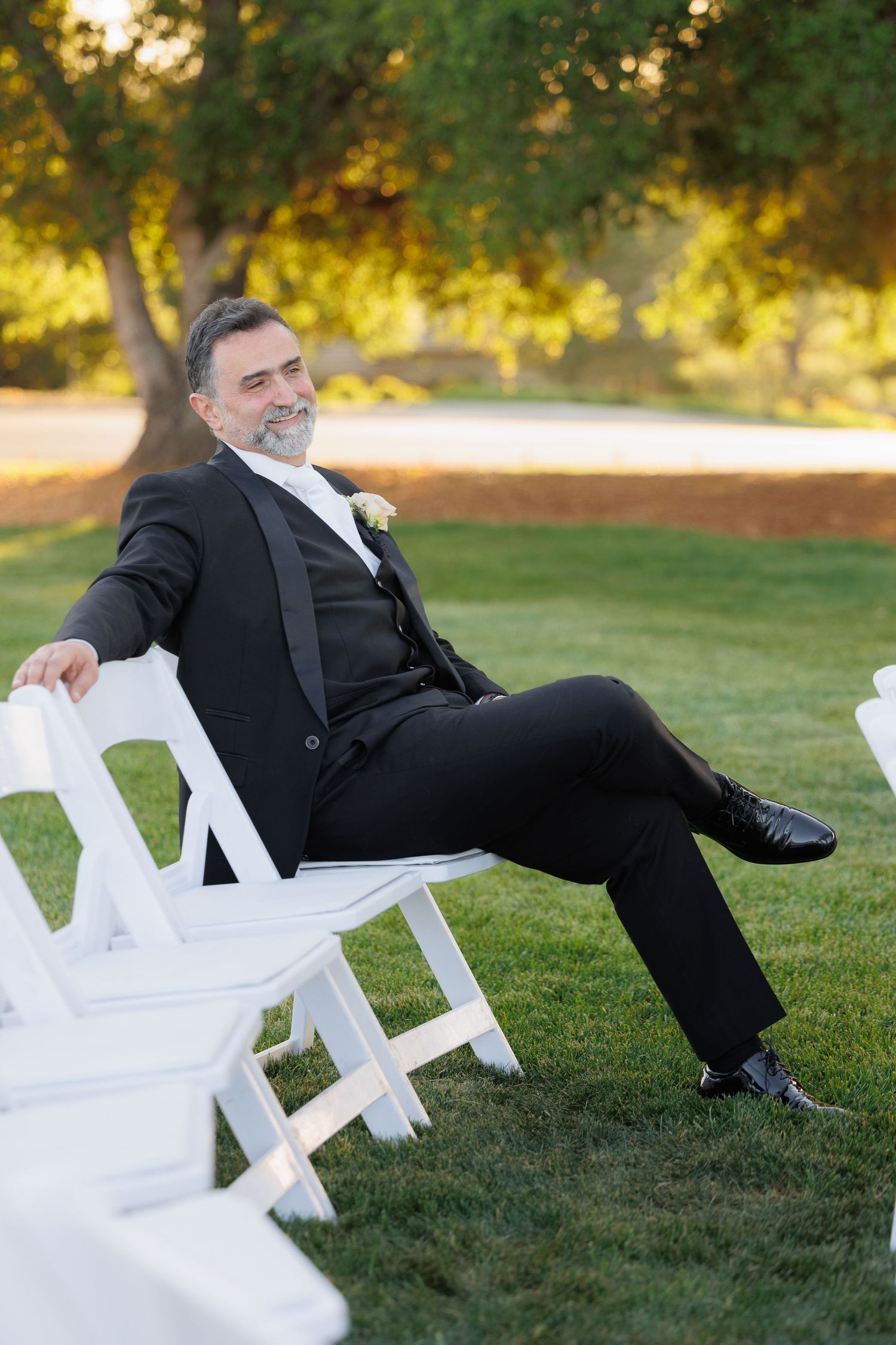A person in a black suit falls backwards off a white chair in a humorous sequence of photos on a grassy lawn.