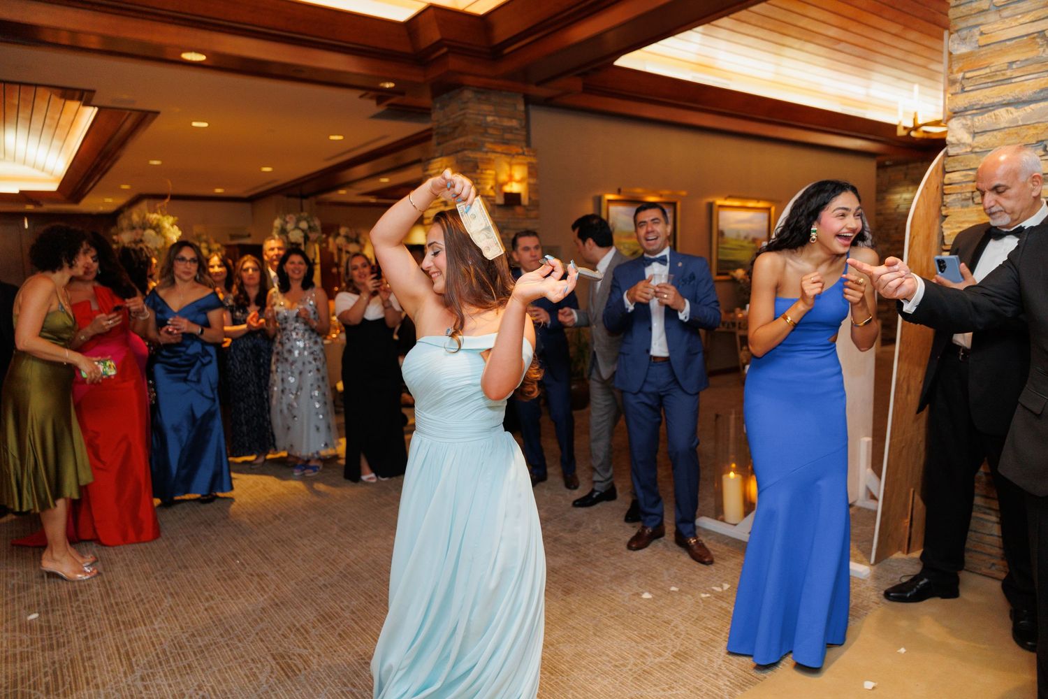 Wedding guests dance and celebrate together during a lively reception in a rustic venue with wooden beams.