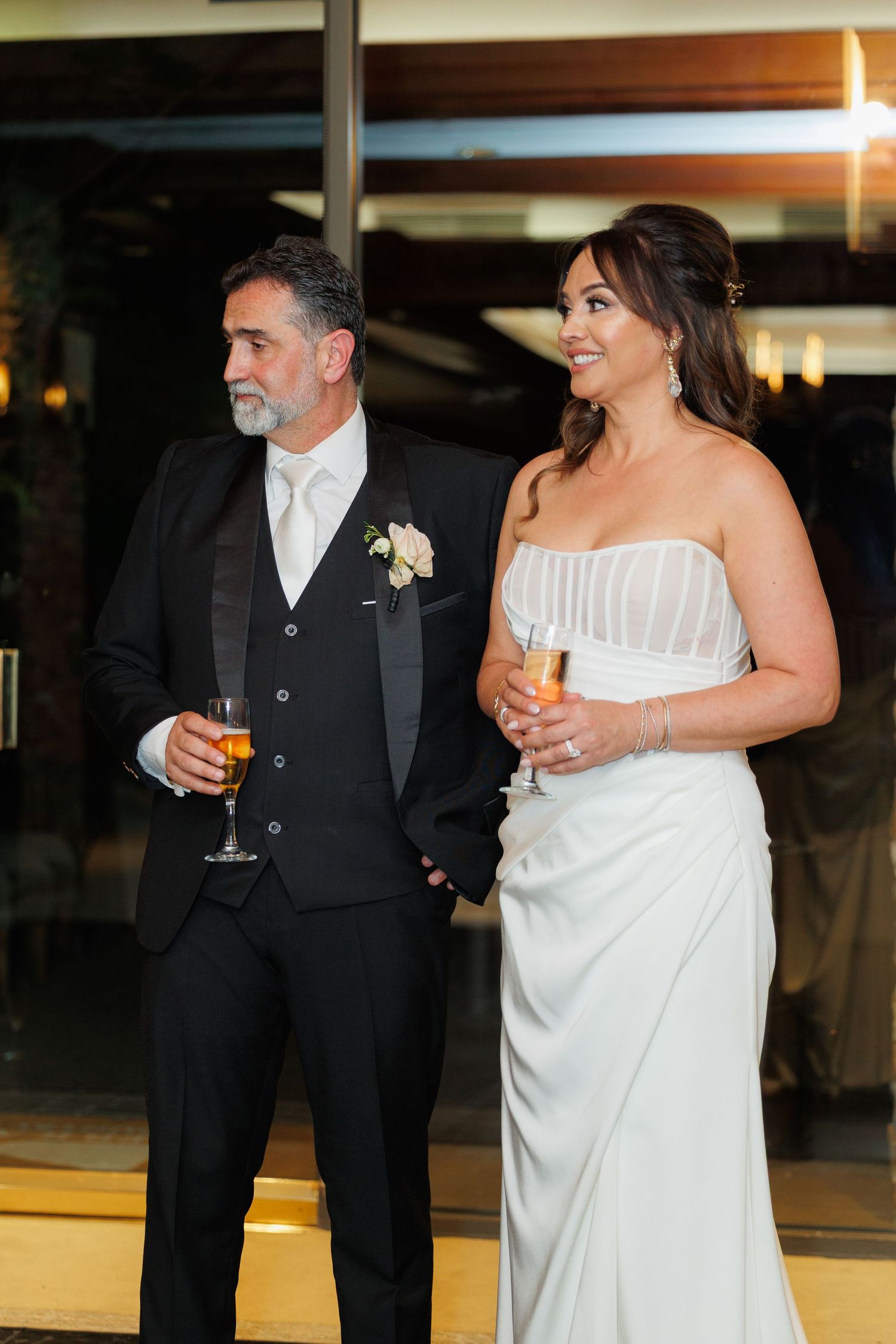 A couple in formal wedding attire, with the bride in white and groom in black, share a moment during their reception.