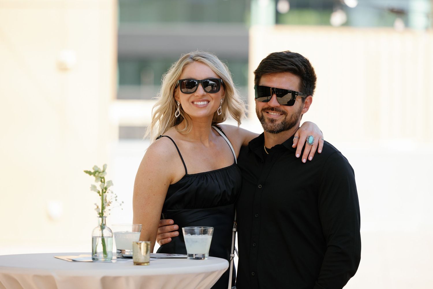 A couple in black outfits pose together in multiple candid shots outdoors on a sunny day.
